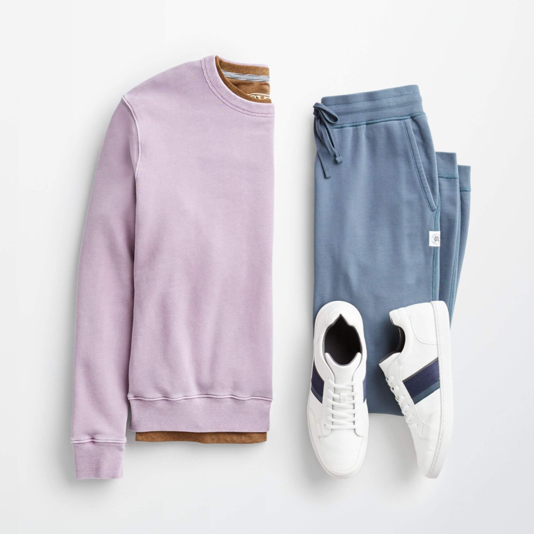 Stitch Fix Men’s outfit laydown featuring a light purple crewneck sweatshirt over a brown t-shirt, next to blue sweatpants and white sneakers. 