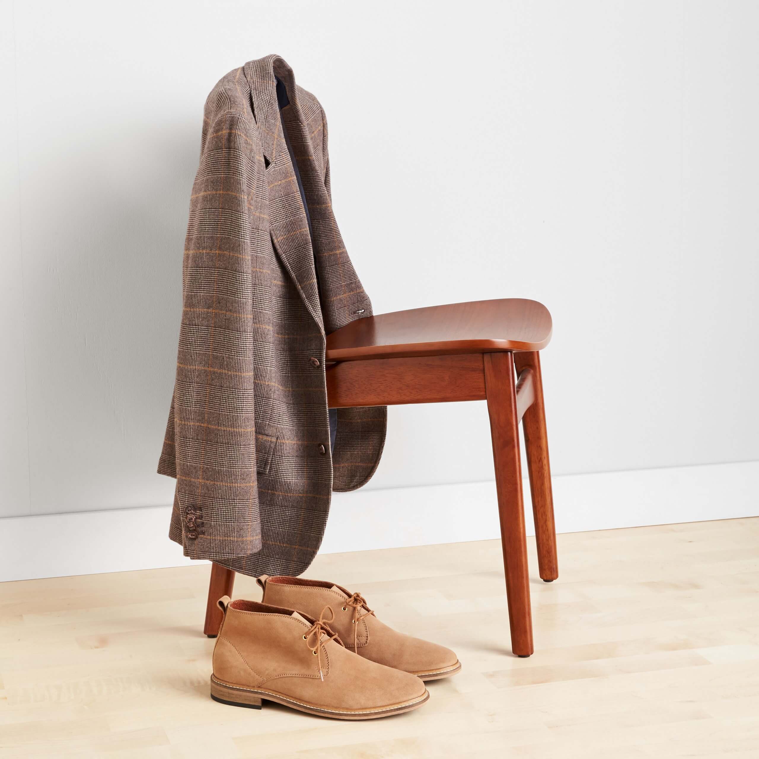 Stitch Fix Men’s brown plaid jacket hanging over a wooden chair, next to tan chukkas on the floor.