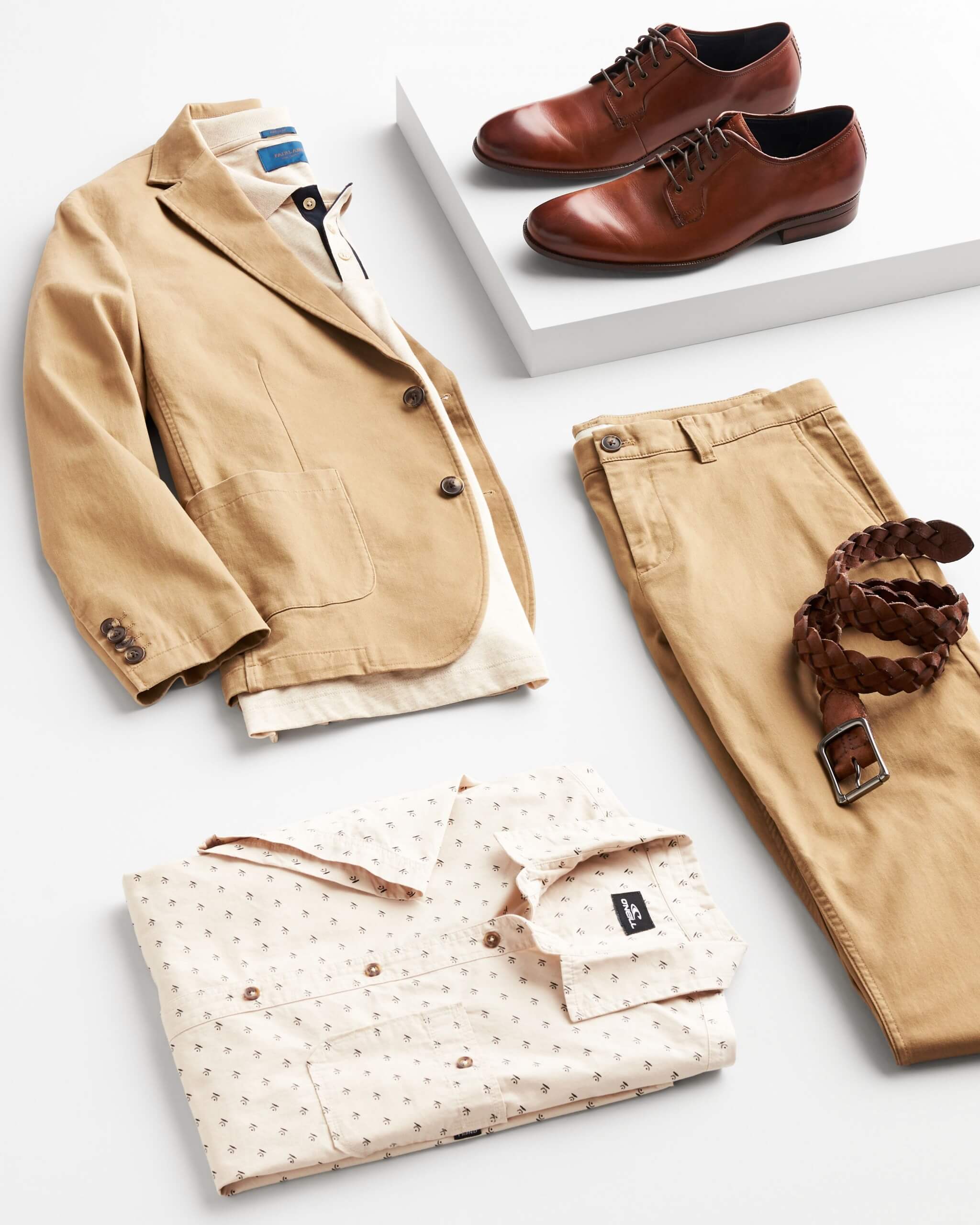 Stitch Fix Men’s outfit laydown featuring cognac Oxford dress shoes on white block next to tan blazer over cream polo shirt, khaki chinos, brown belt and tan folded button-front shirt. 