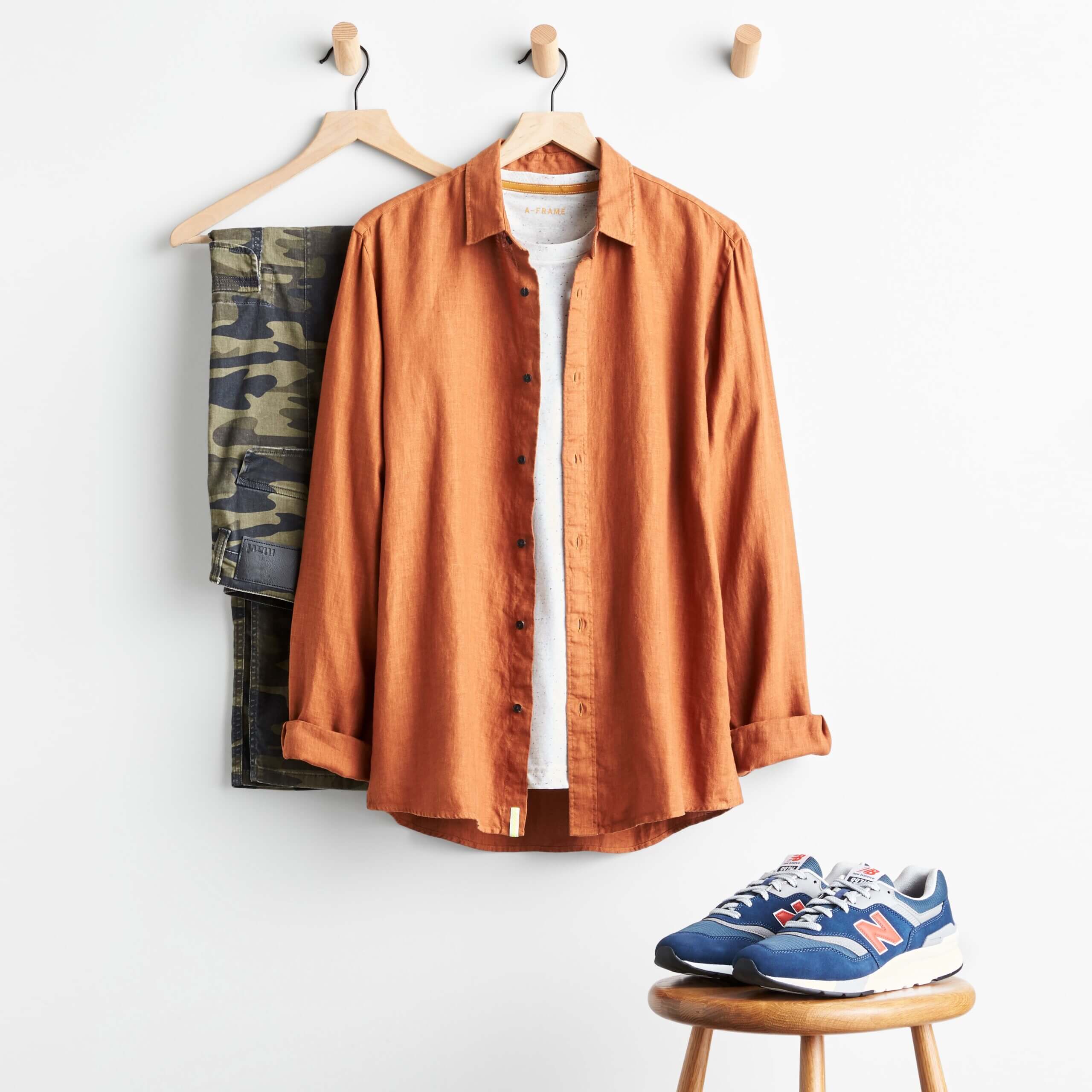 Stitch Fix Men’s camouflage pants, white T-shirt, orange button-up and navy and orange sneakers.