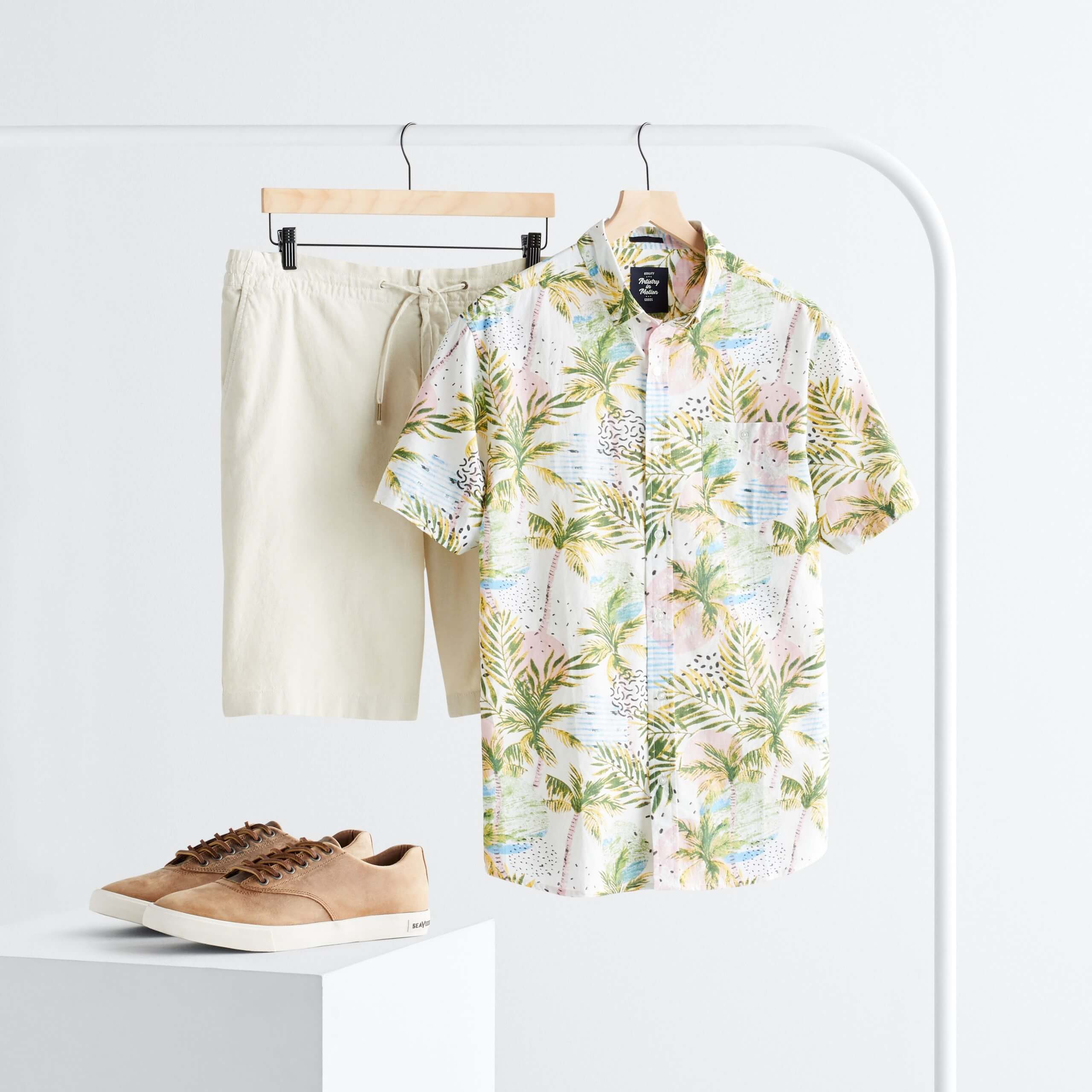 Stitch Fix Men’s rack image with white, green and pink tropical print button-down short sleeve shirt and cream shorts hanging on white rack next to brown leather sneakers on white block.