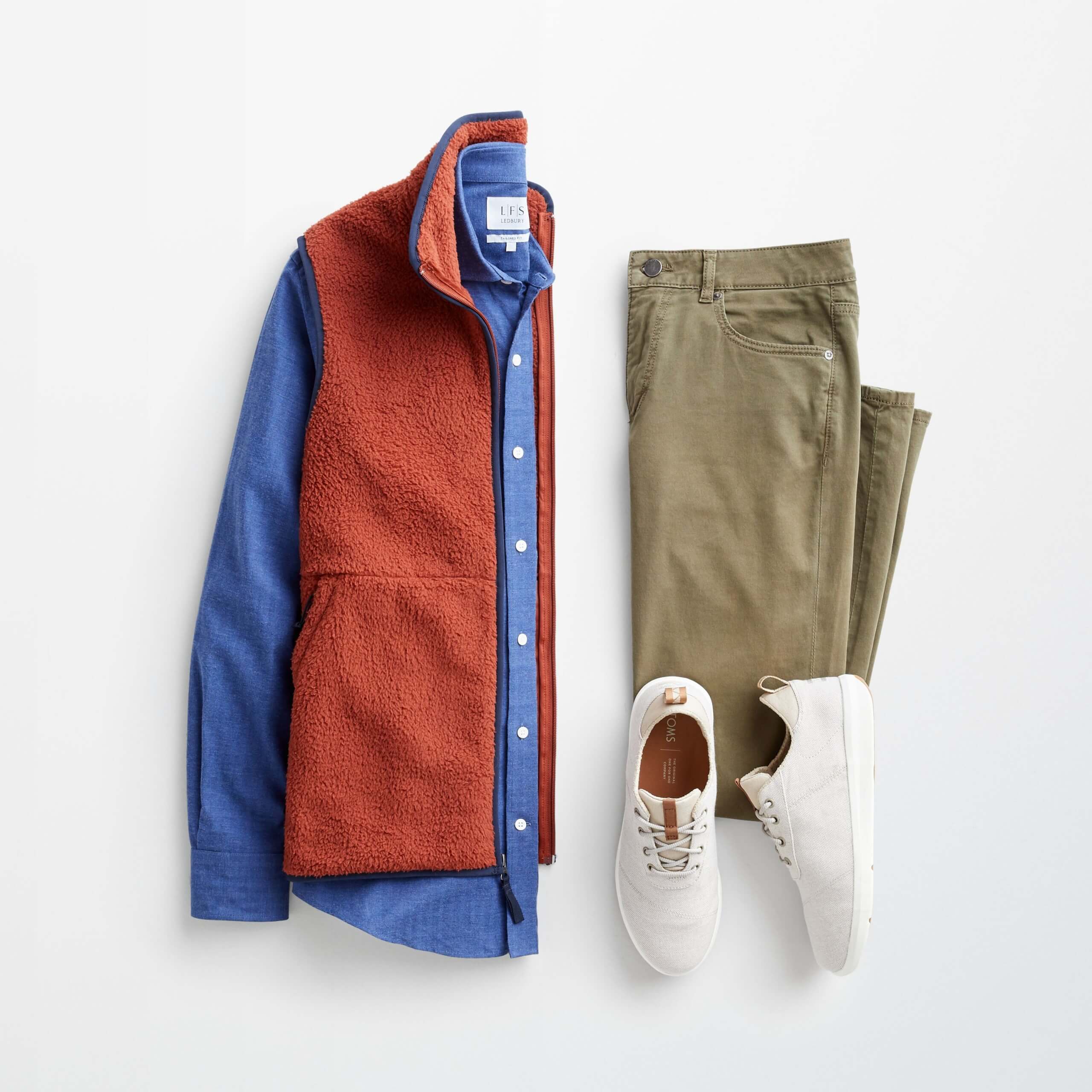 Stitch Fix Men's outfit laydown featuring an orange vest over a blue long sleeve button-down shirt, olive green jeans and cream lace-up sneakers. 