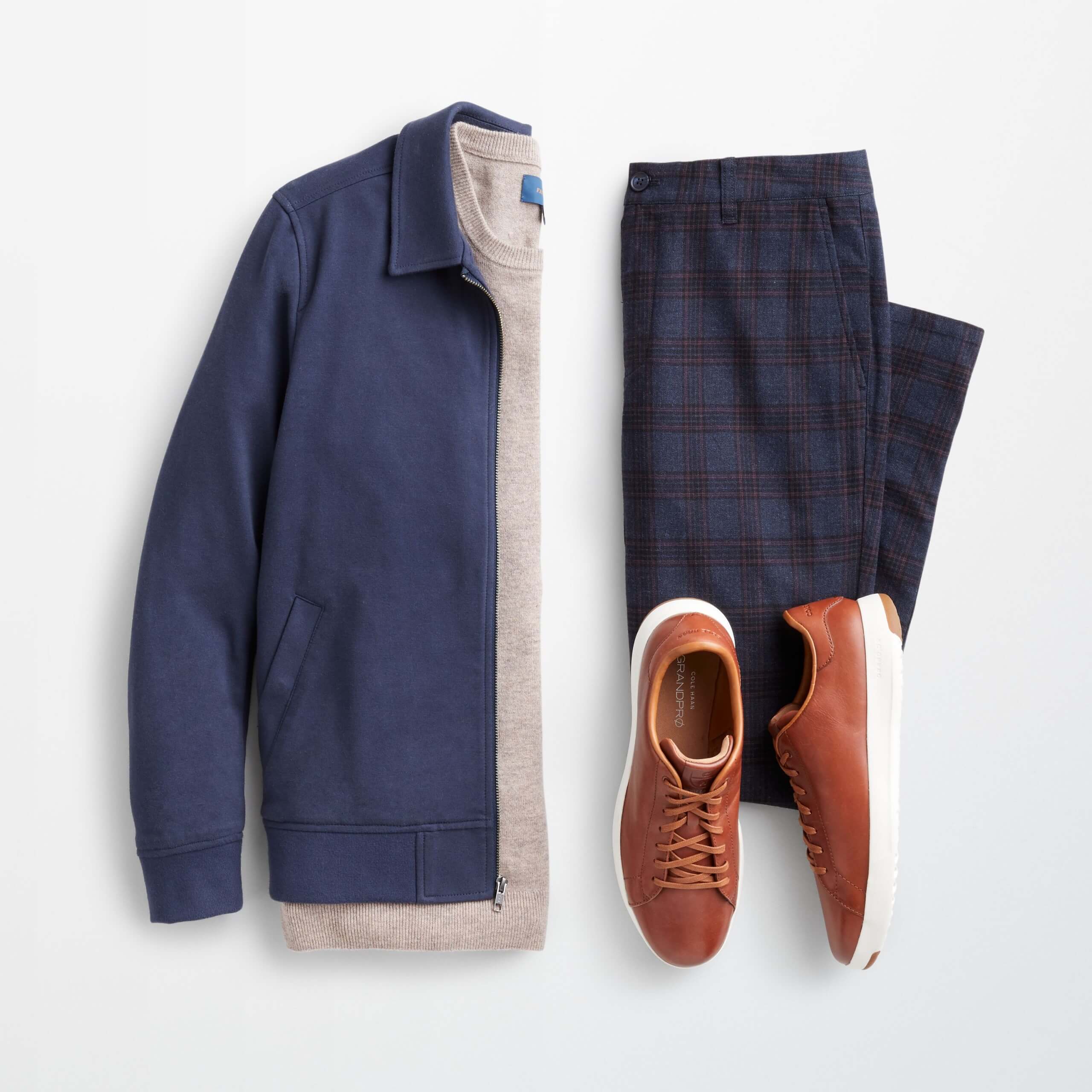 Stitch Fix Men’s outfit laydown featuring navy harrington jacket over cream pullover sweater next to navy plaid chinos and brown leather sneakers. 