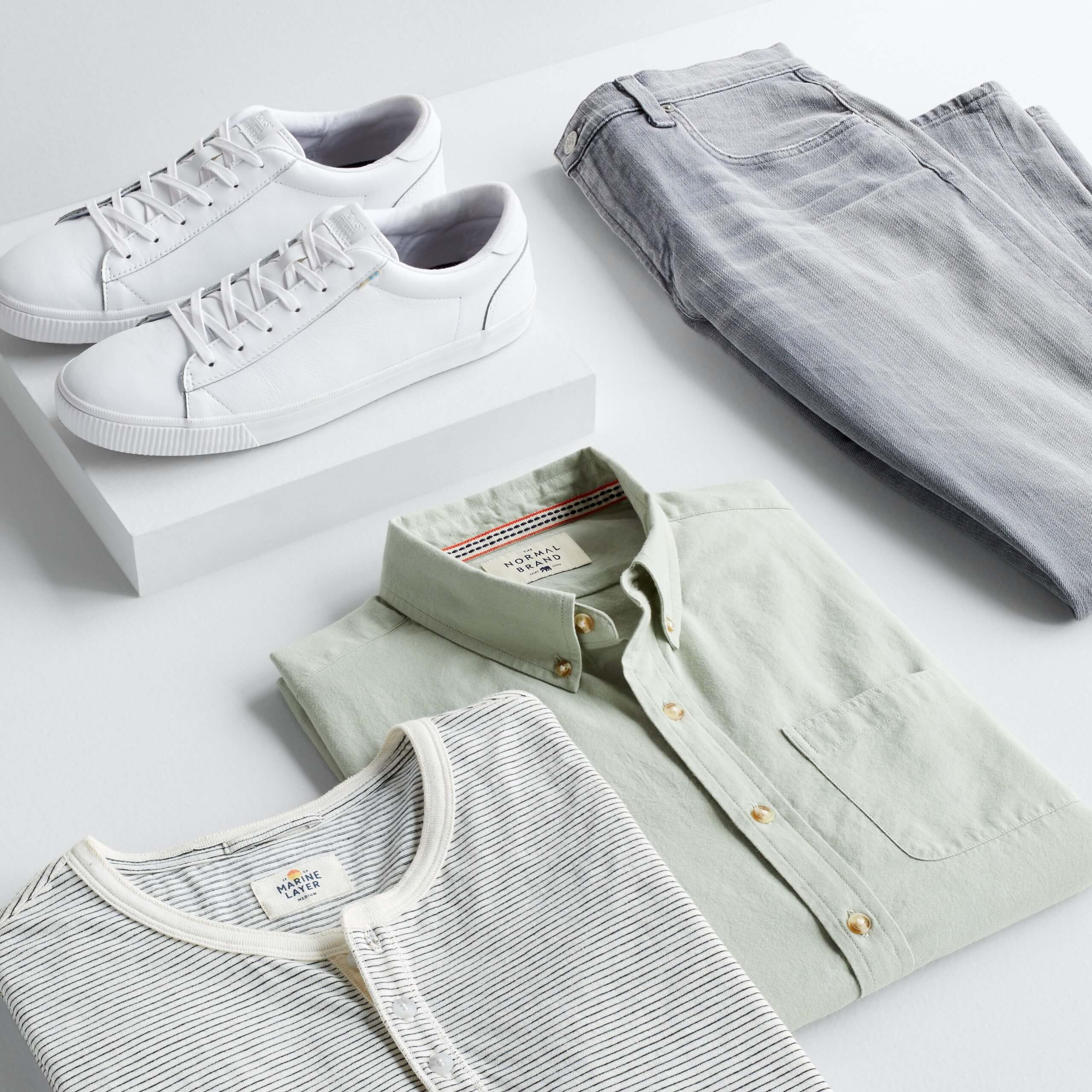 Stitch Fix Men's outfit laydown featuring white and grey striped henley shirt, sage green long sleeve button-down shirt and grey jeans next to white sneakers on a white block.