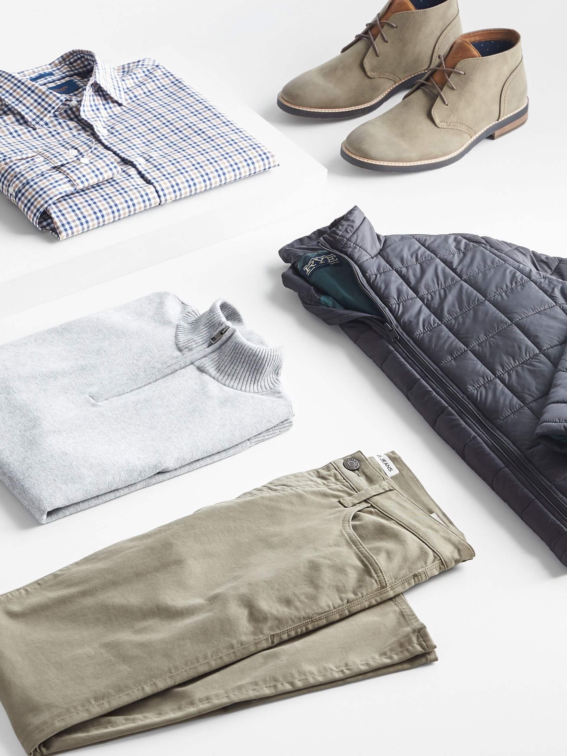 Stitch Fix Men’s outfit laydown featuring white and blue button-down shirt, beige chukkas, grey quarter-zip pullover, olive-green pants, and black puffer jacket. 