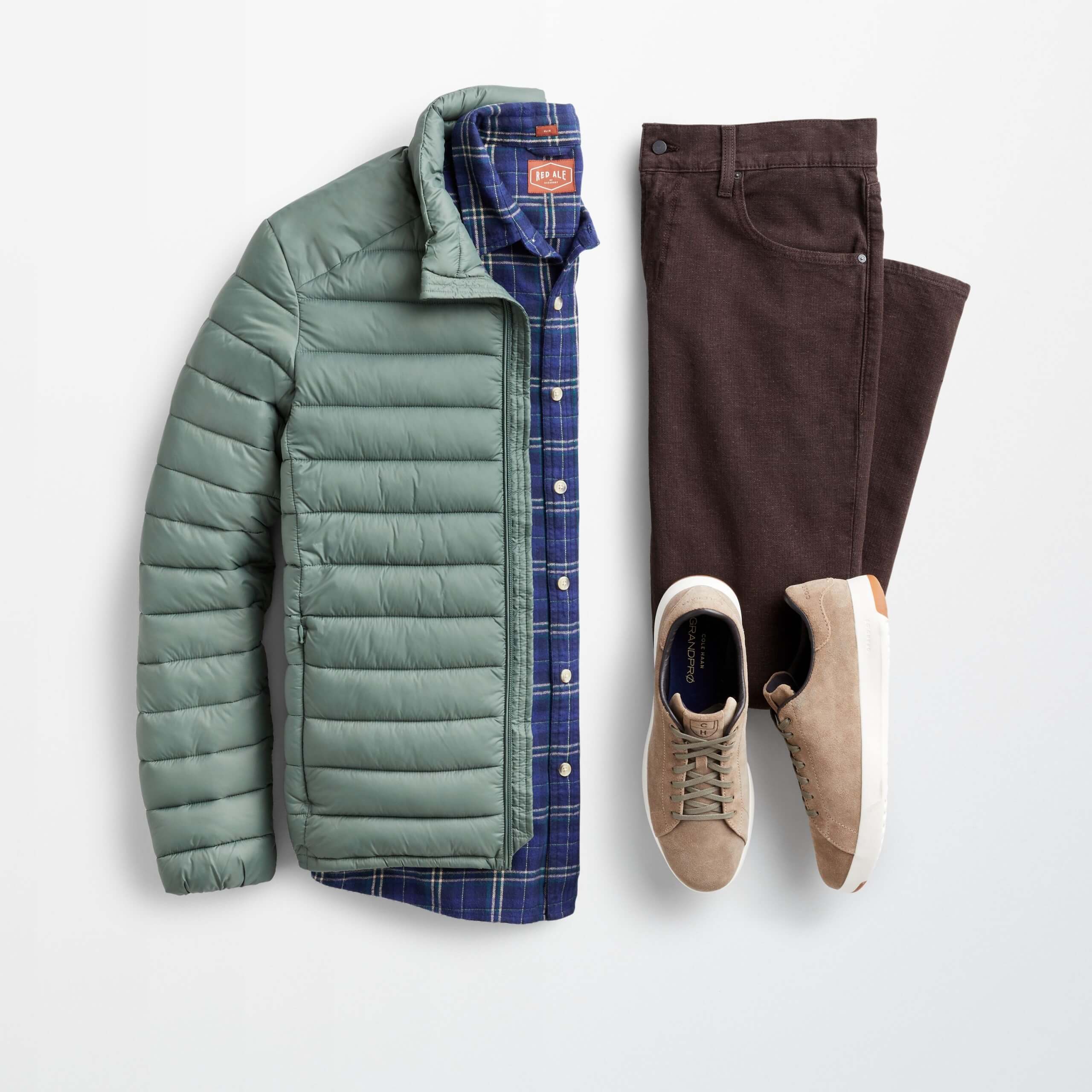 Stitch Fix Men’s outfit laydown featuring green puffer jacket over navy plaid button-down shirt, brown pants and tan suede sneakers. 