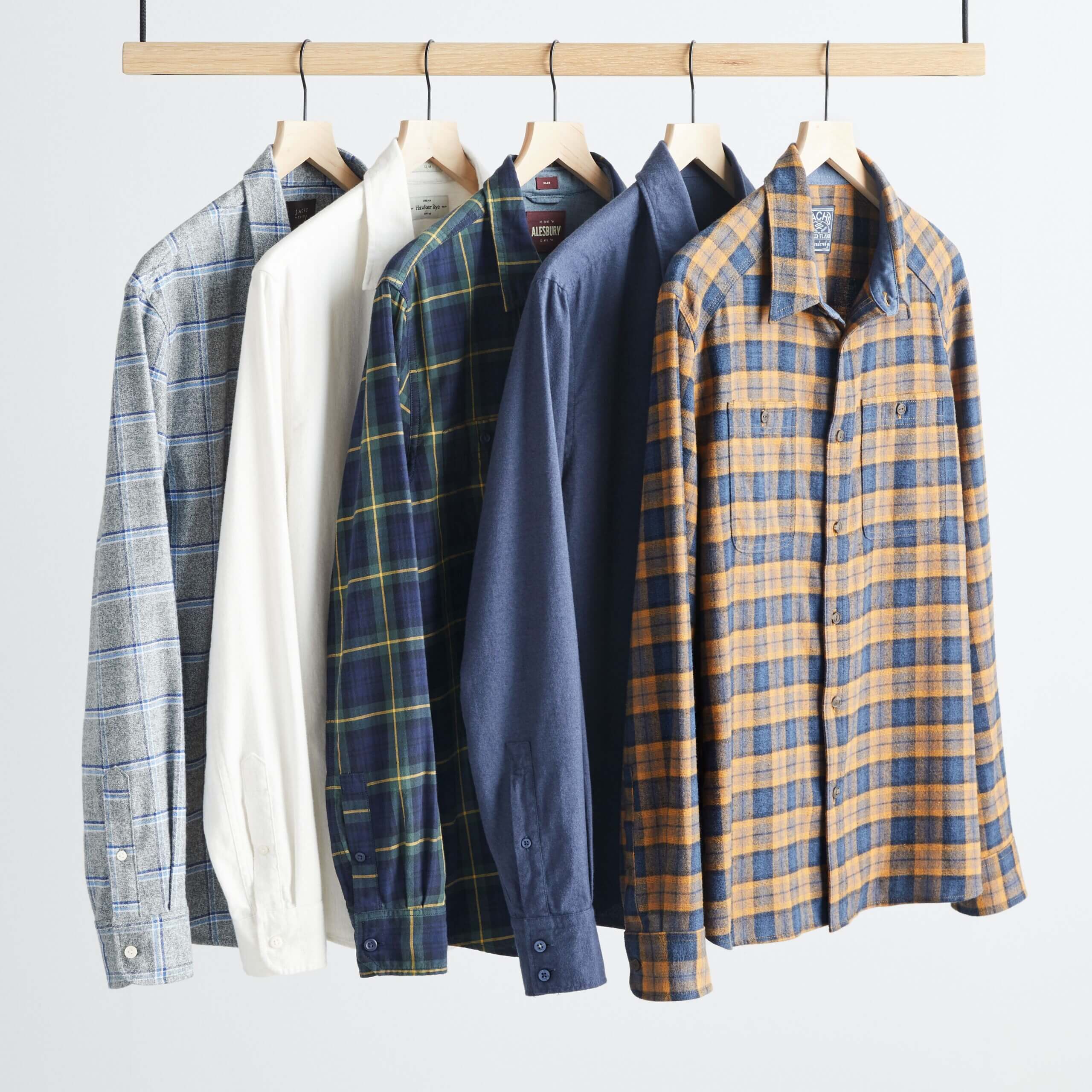 Stitch Fix men's assortment of flannel shirts hanging on wooden rack in various colors. 