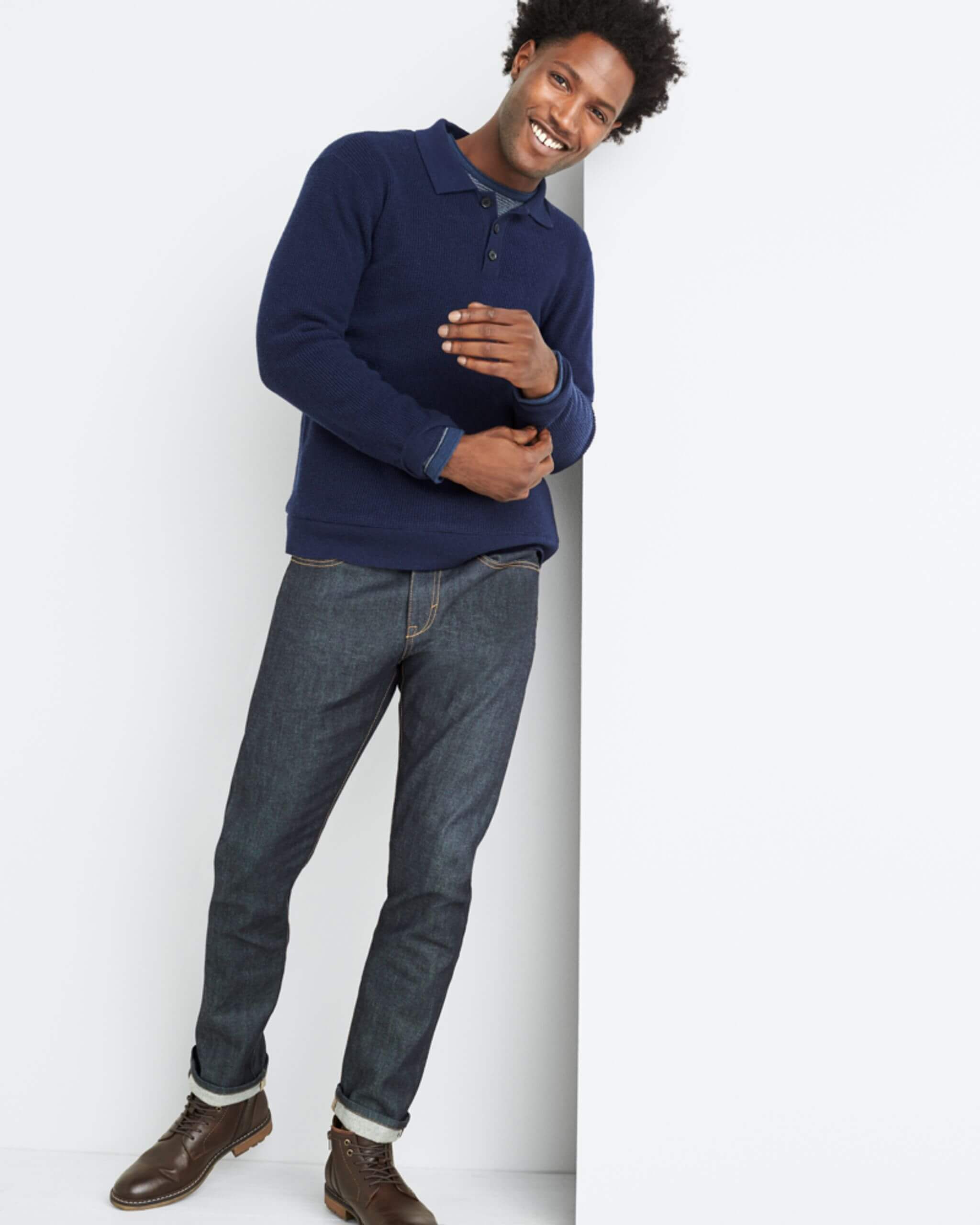 Stitch Fix Men’s model standing wearing navy polo sweater over navy crew neck shirt with slim-fit jeans and brown combat boots.