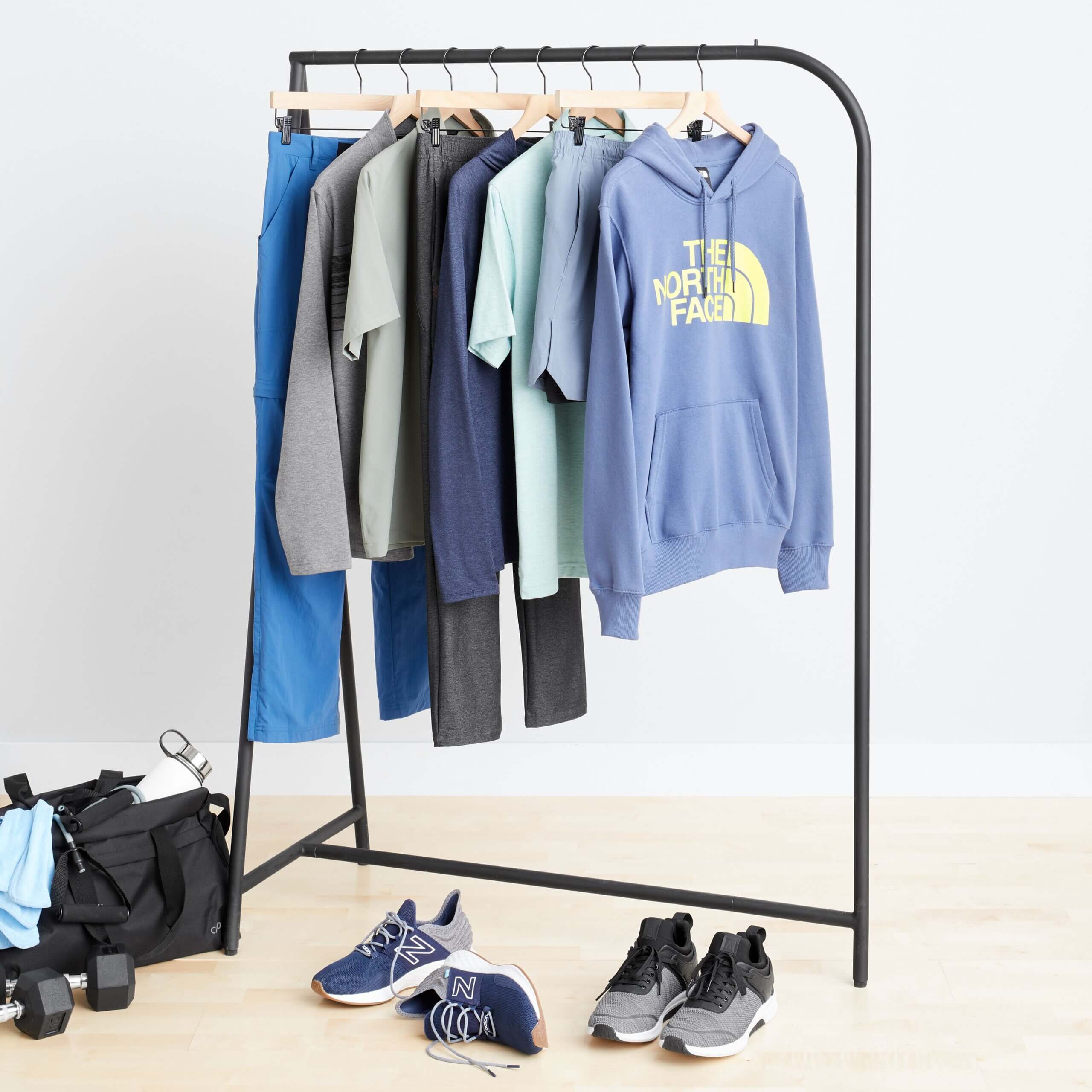 Stitch Fix men's rack image featuring blue hoodie, blue shorts, light short sleeve shirts and blue pants, next to various active sneakers in grey and navy, as well as weights on the floor.