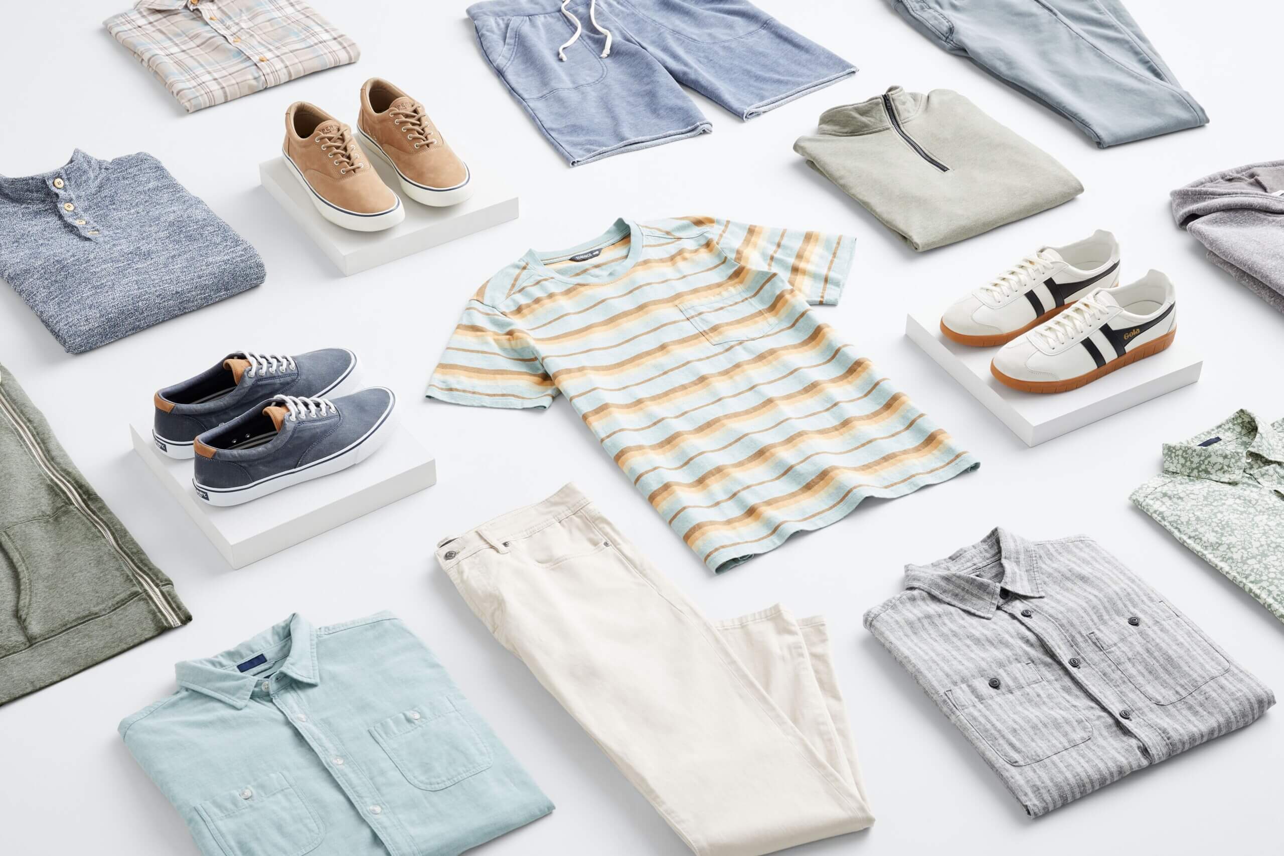 Stitch Fix men's laydown featuring blue shorts, light jeans, khaki jeans, various light blue shirts in henley and button-down styles, sneakers in white, blue and tan. 