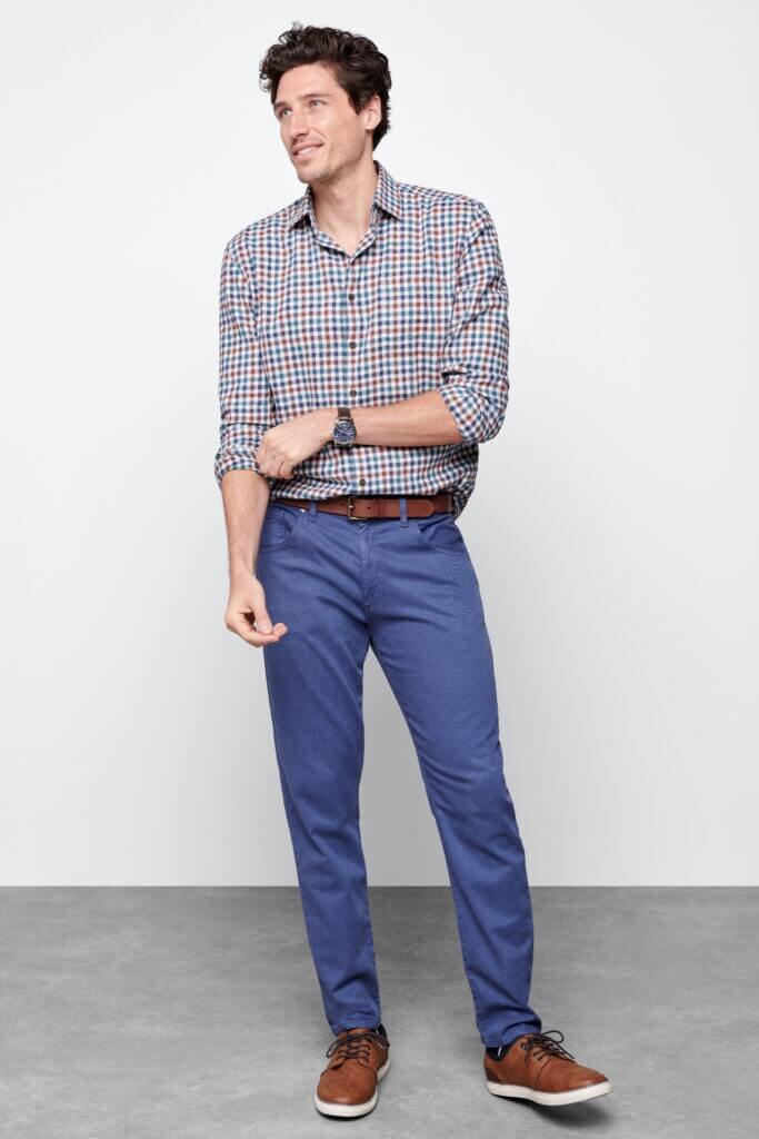 Stitch Fix model wearing men’s broad shoulder outfit with plaid shirt, brown belt, blue pants and brown sneakers.