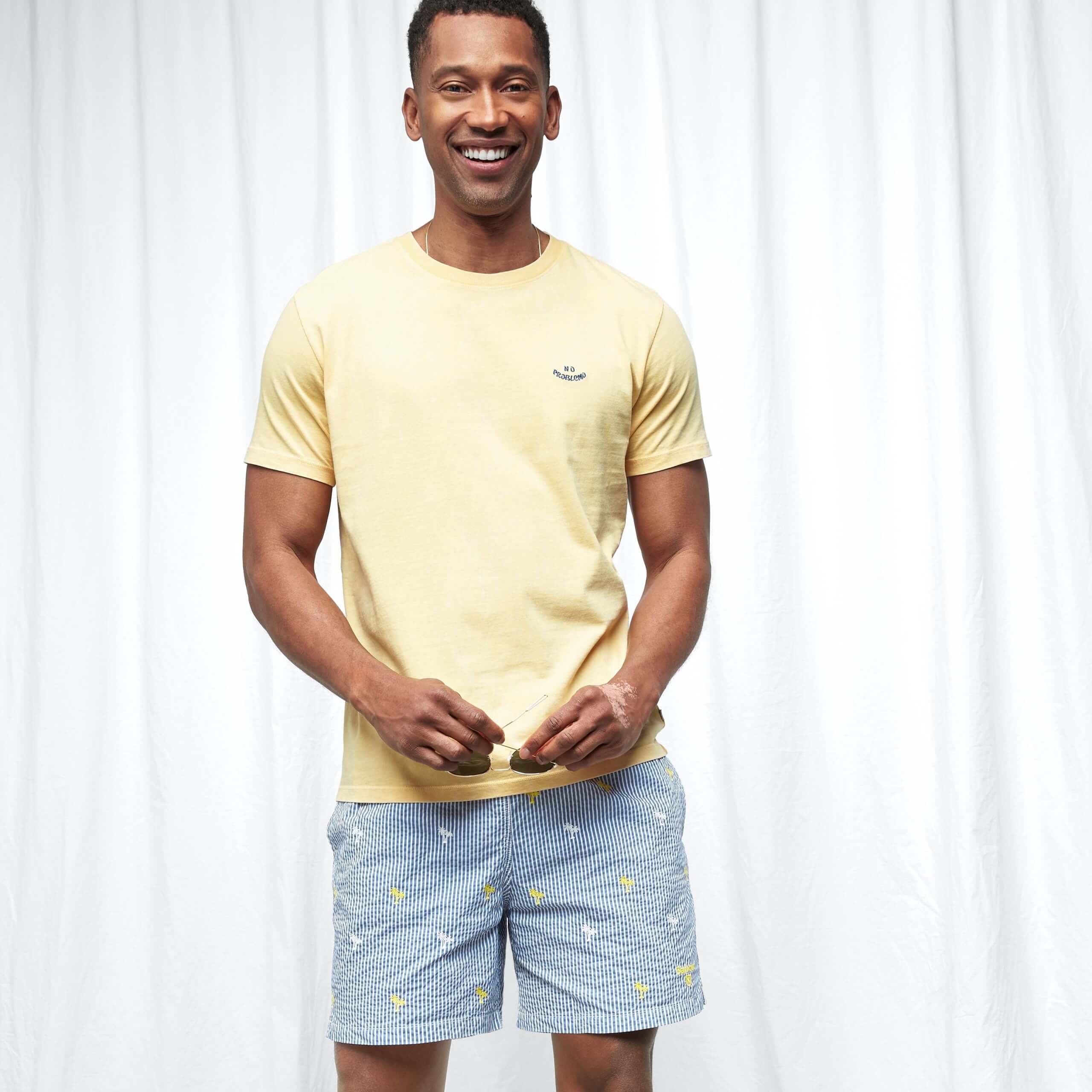 Stitch Fix Men's model wearing yellow t-shirt and blue shorts with palm tree details. 