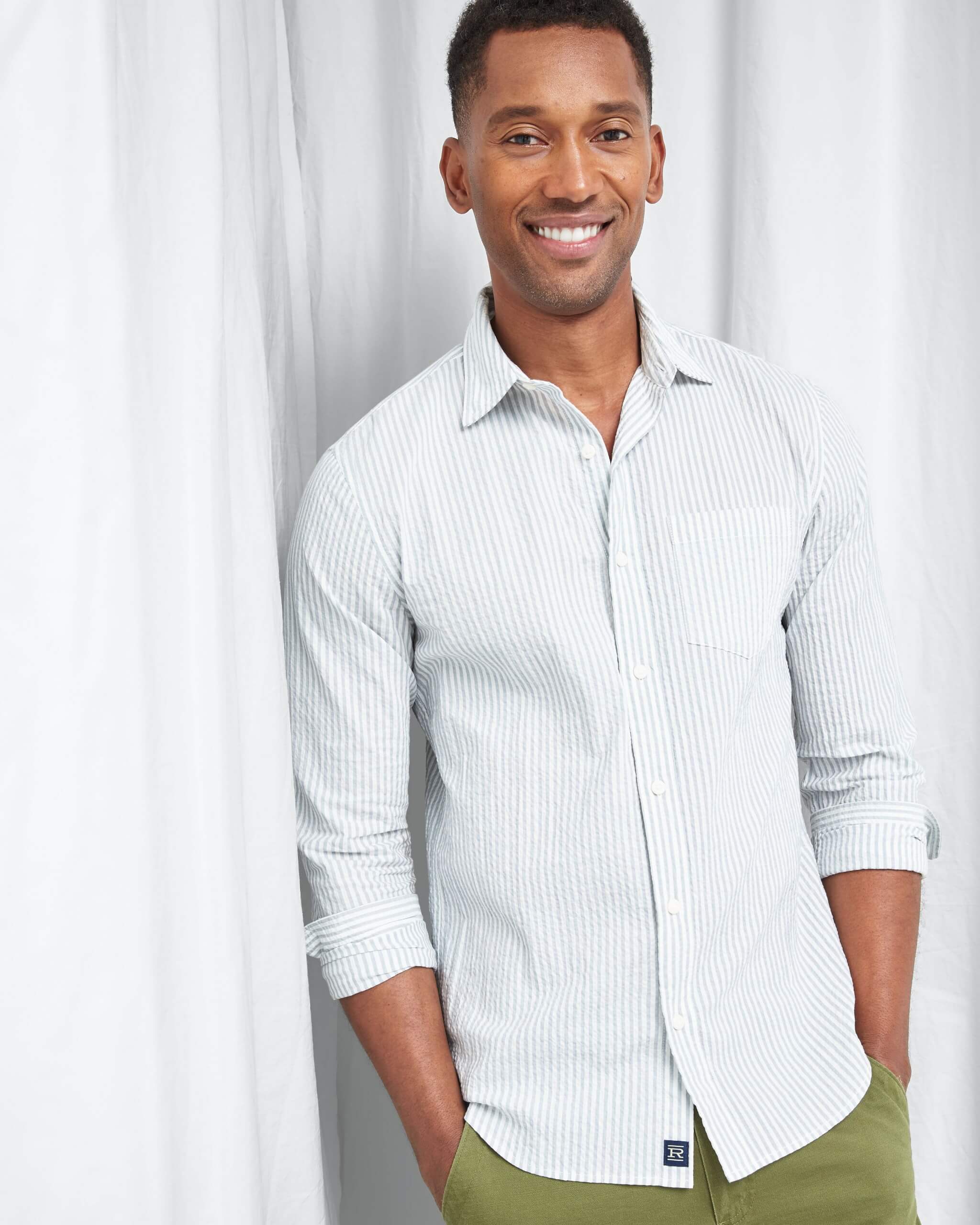 Stitch Fix Men's model standing wearing white and light blue striped button-down shirt and green pants.