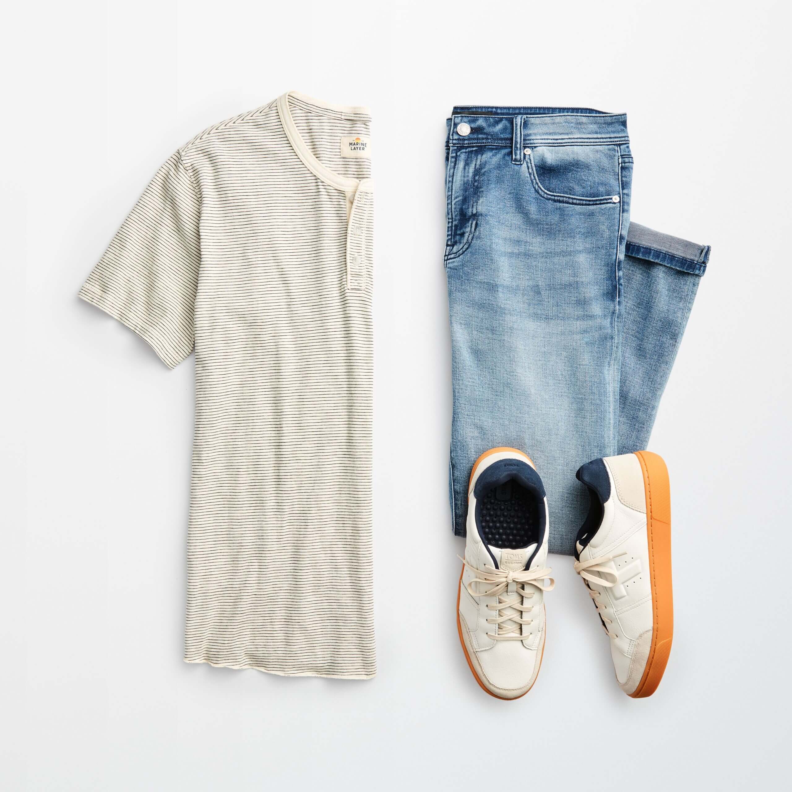 Stitch Fix Men’s outfit laydown featuring white striped henley shirt, blue jeans and white sneakers.