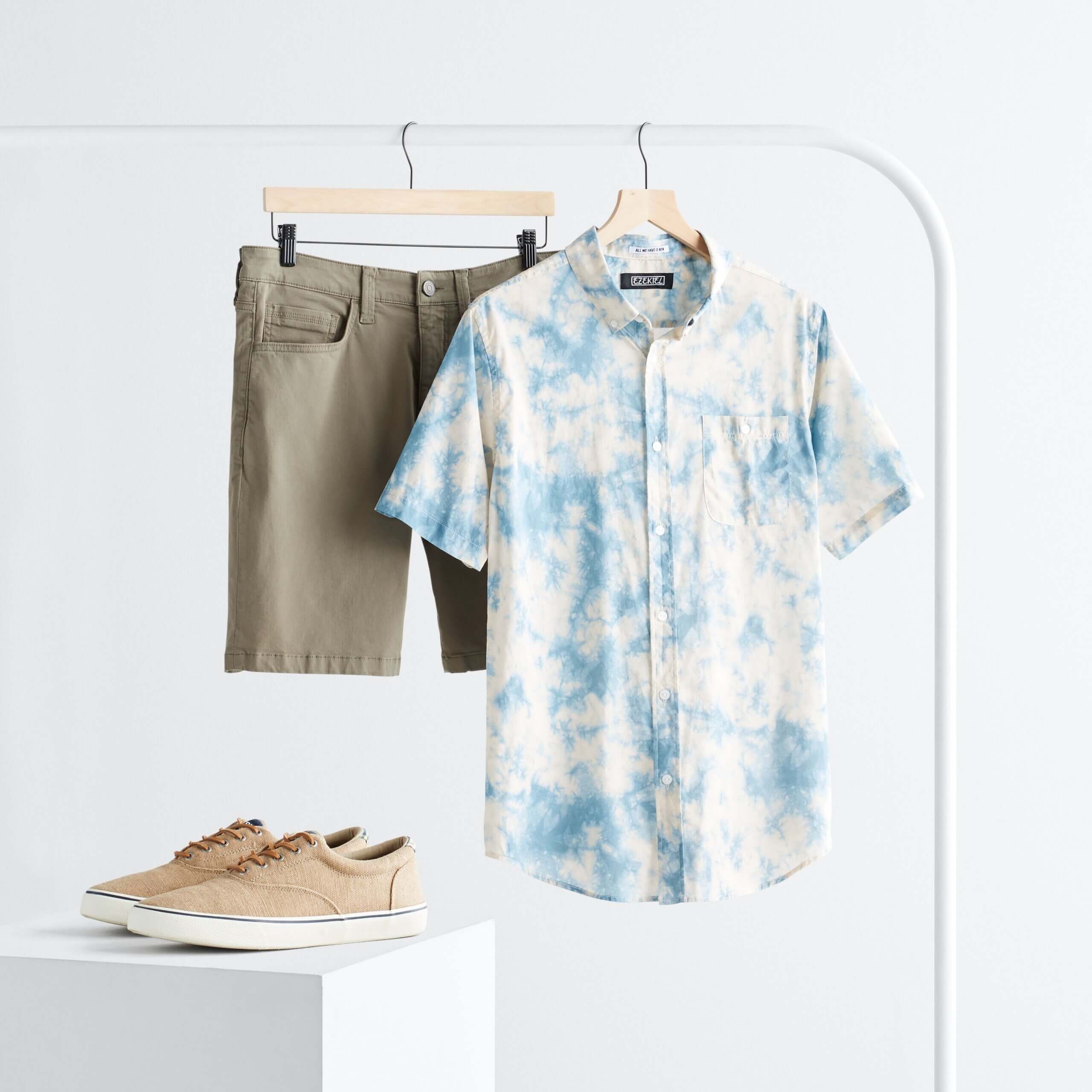 Stitch Fix men’s rack image with blue tie-dye button-down short sleeve shirt and olive shorts hanging on white rack next to tan leather sneakers on white block.