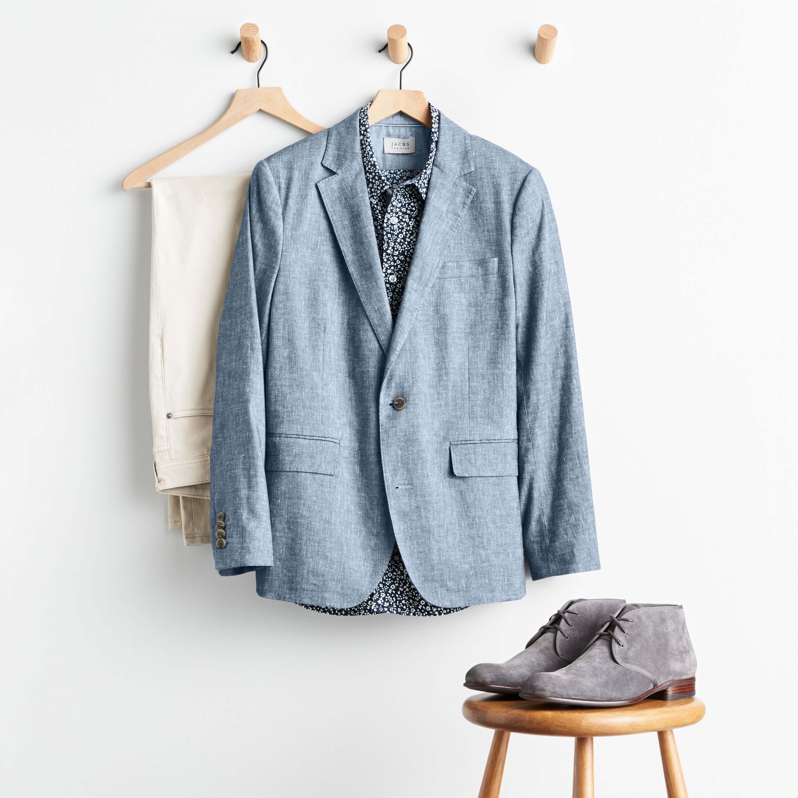 Stitch Fix men’s outfit including chambray blazer, floral button-down shirt, beige pants and grey chukkas on a stool.