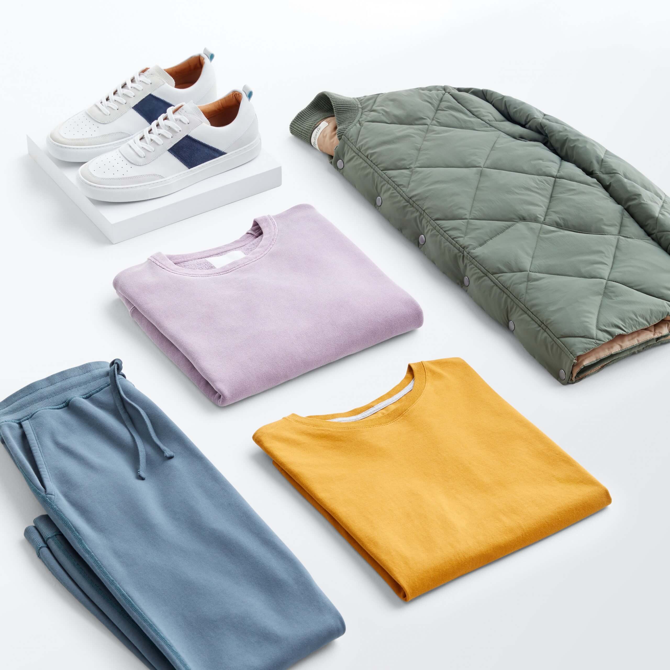 Stitch Fix men’s outfit laydown featuring blue joggers, light purple T-shirt, yellow sweatshirt, olive green bomber jacket and white sneakers.
