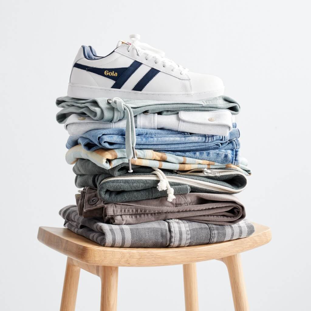 Stitch Fix men’s stacked folded clothing on a stool with white and navy lace-up sneakers on top.