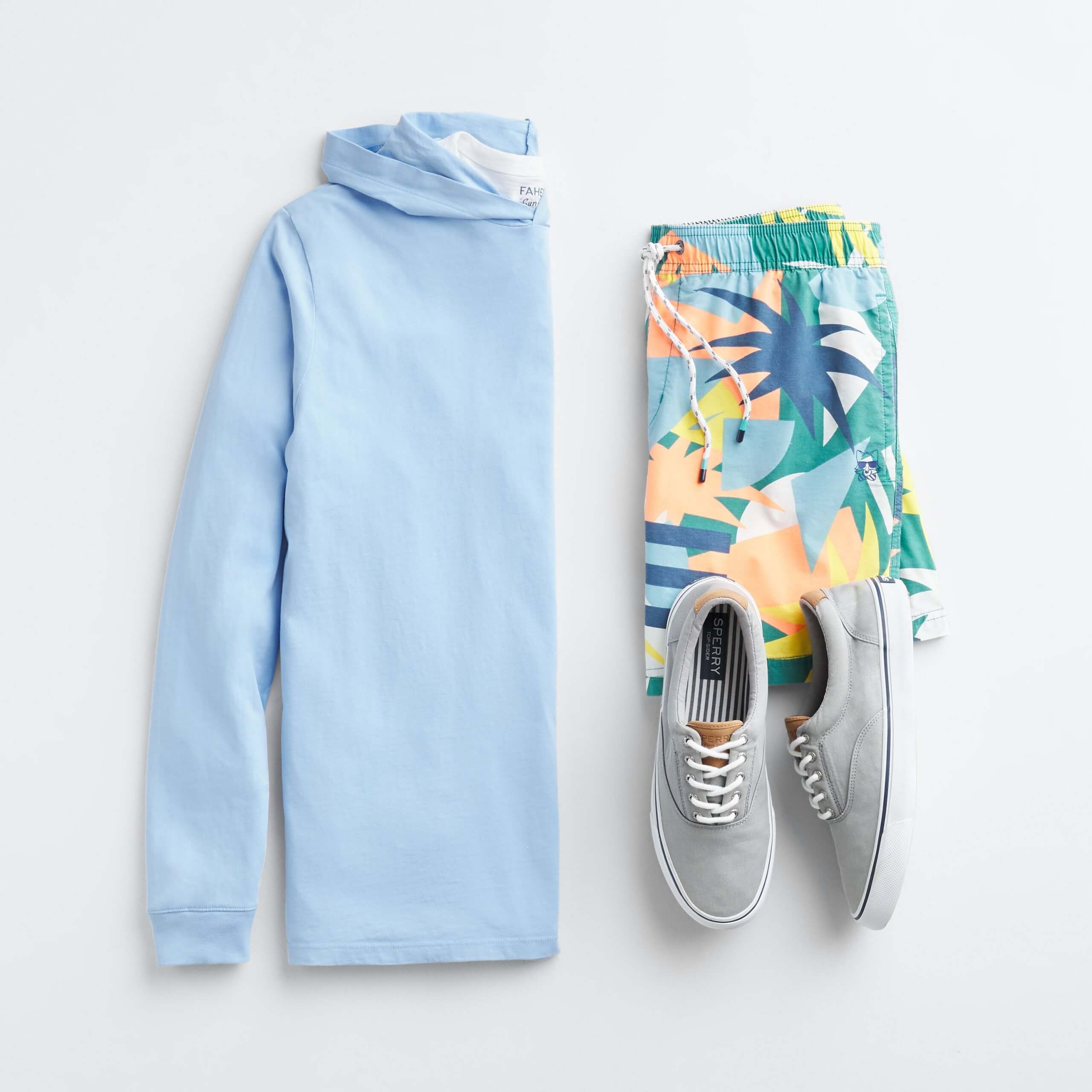 Stitch Fix Men’s outfit laydown featuring a blue hoodie, multi-colored tropical board shorts and grey lace-up sneakers.