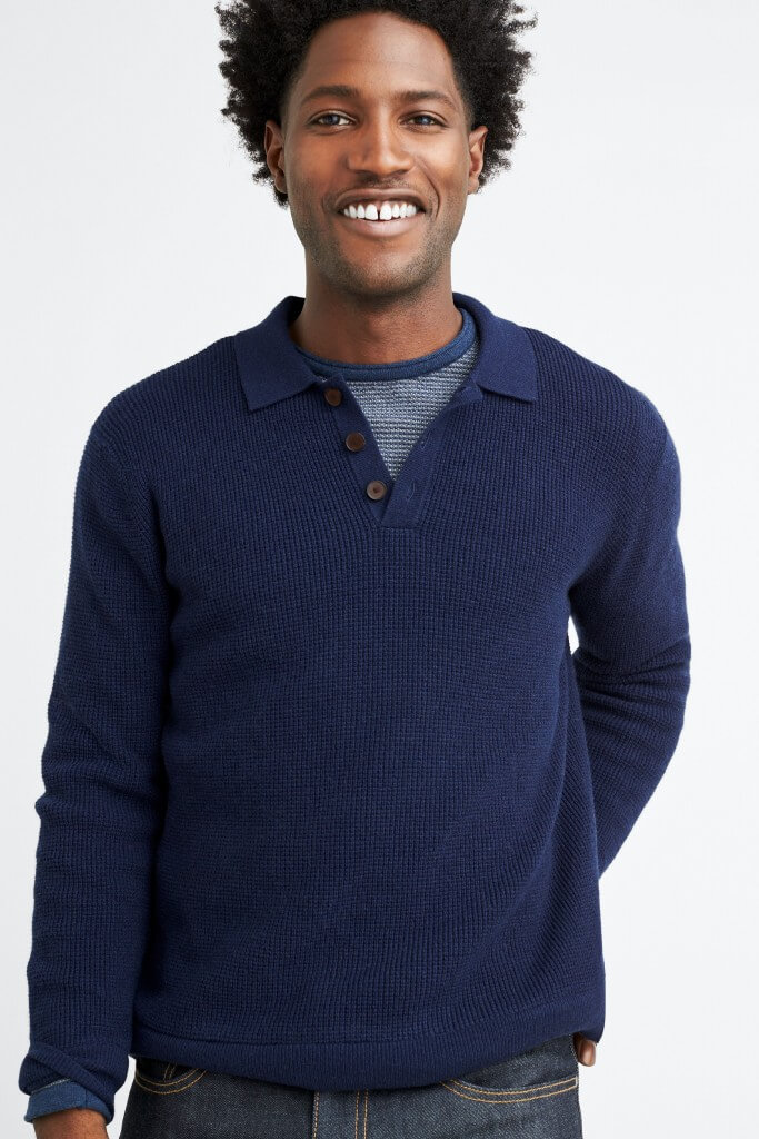 Stitch Fix model in a men’s navy quarter-button sweater over a striped blue crew neck and dark wash jeans.