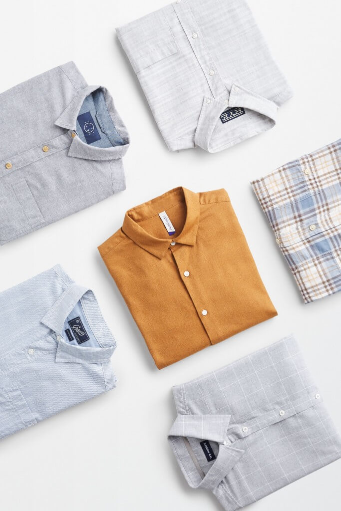 Stitch Fix men’s folded button-up shirts in solid grey, plaid shirts and a solid orange shirt.