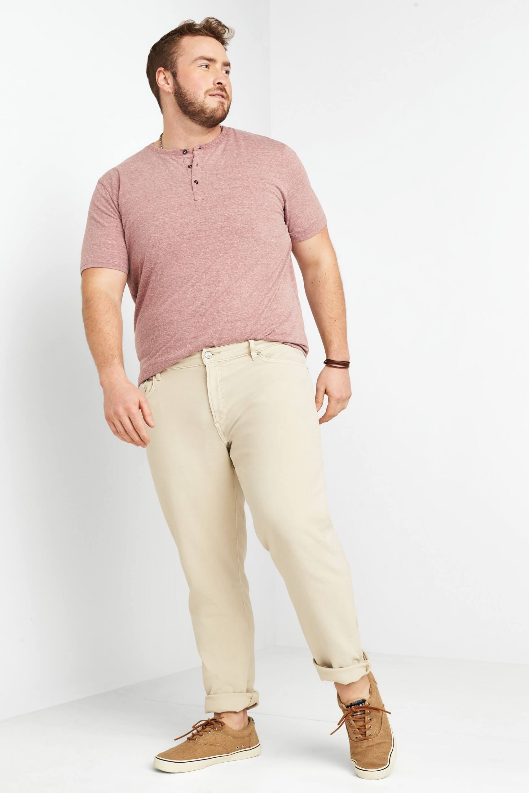 Stitch Fix model wearing men’s pink heathered short-sleeve henley with beige cuffed jeans, brown woven bracelets and tan sneakers.