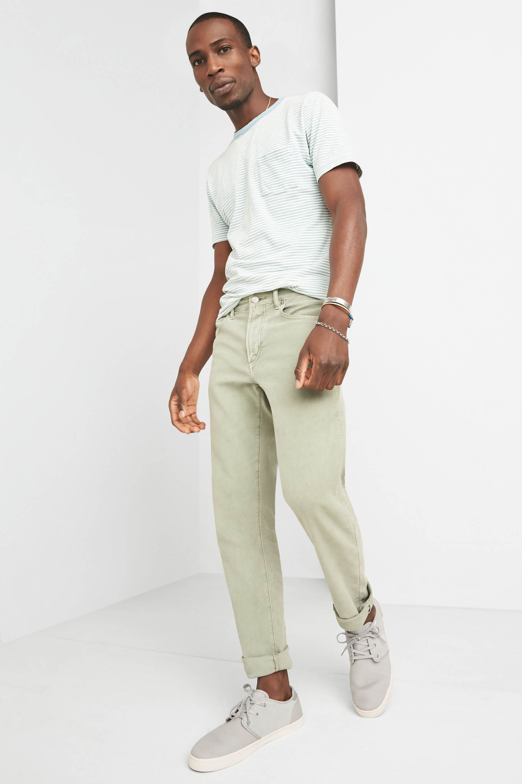 Stitch Fix model wearing men’s blue and white striped T-shirt with light green cuffed jeans, grey sneakers and silver bracelets.