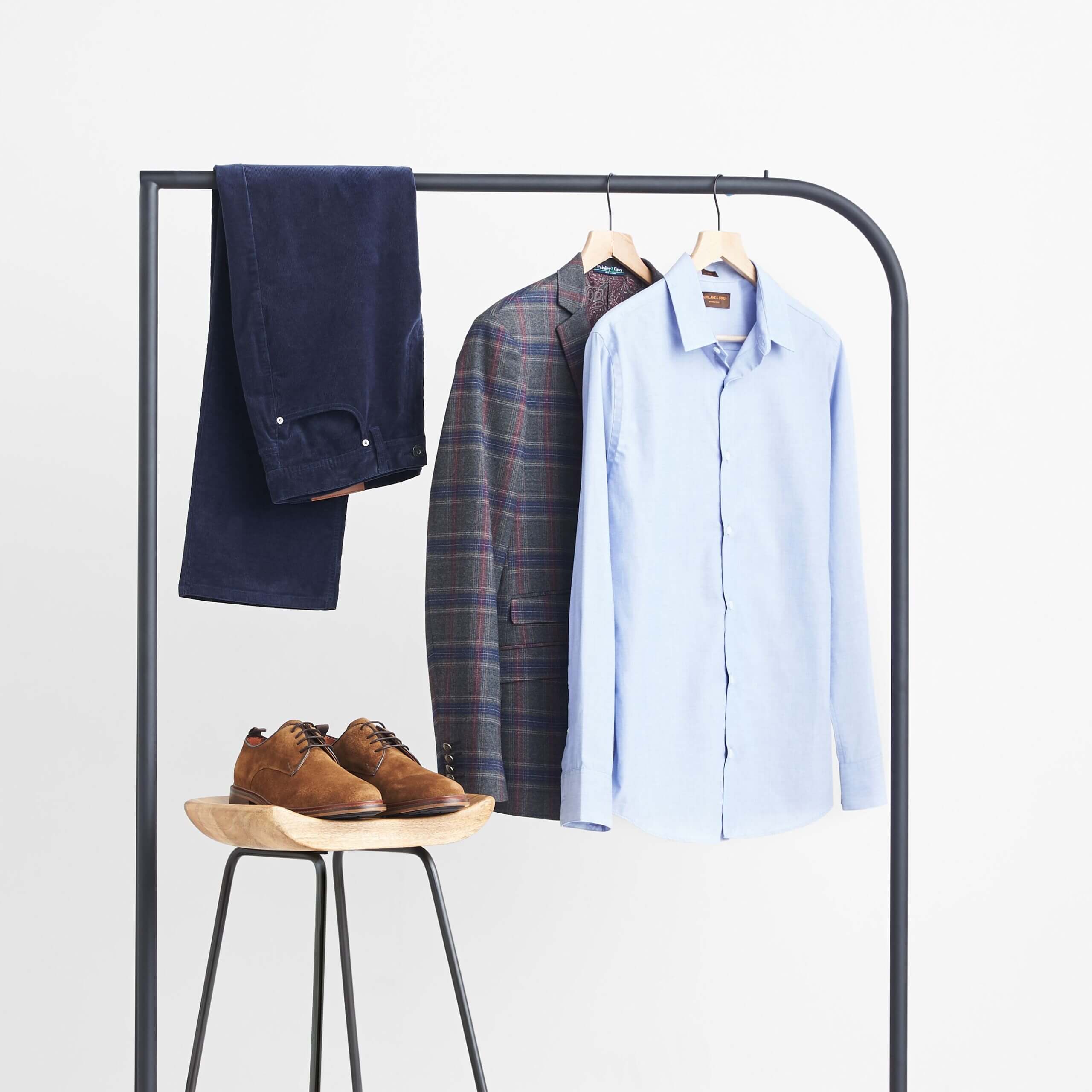 Stitch Fix workleisure outfit featuring navy cords, blue button-down shirt, plaid blazer on rack with brown oxford shoes on stool.