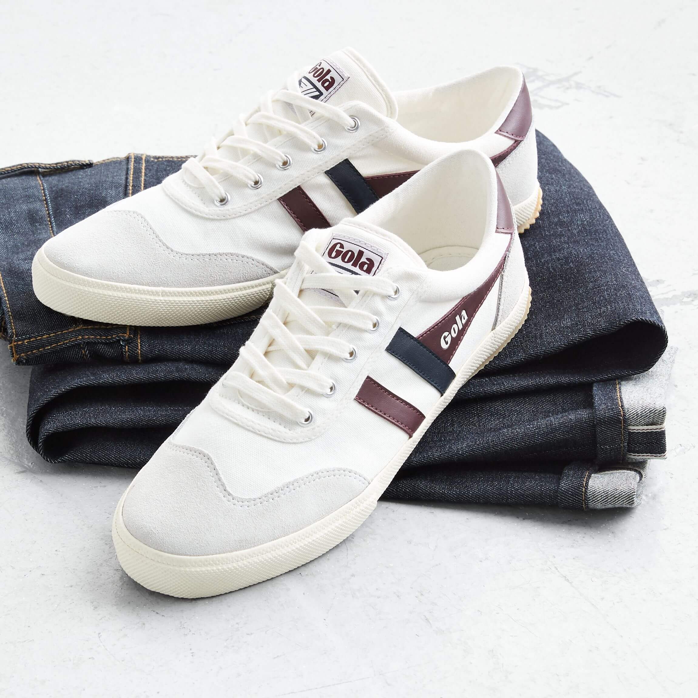 Stitch Fix men’s white, burgundy and black sneakers on top of folded dark-wash jeans.