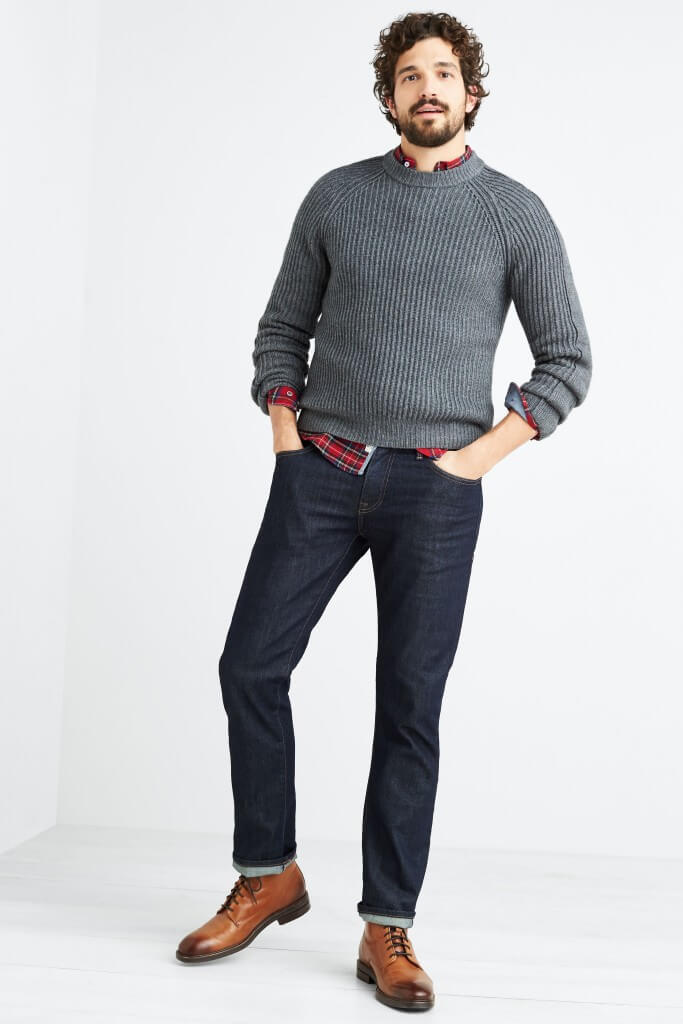 Stitch Fix men’s model wearing red plaid button-up layered under a grey crew neck sweater, dark jeans and brown lace-up boots.