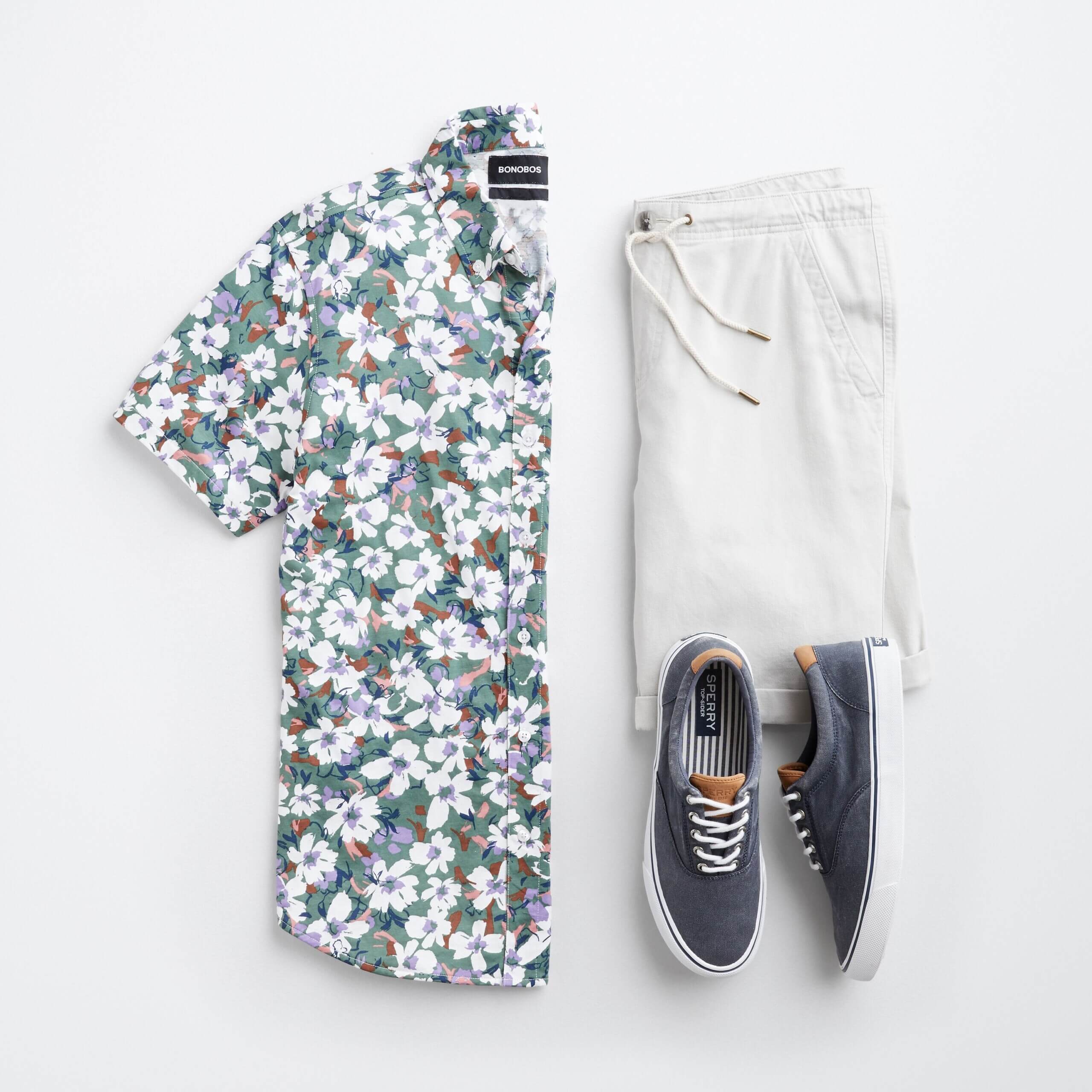 Stitch Fix men’s resort outfit featuring multi-colored short-sleeve button-down tropical shirt, white drawstring shorts and navy sneakers.