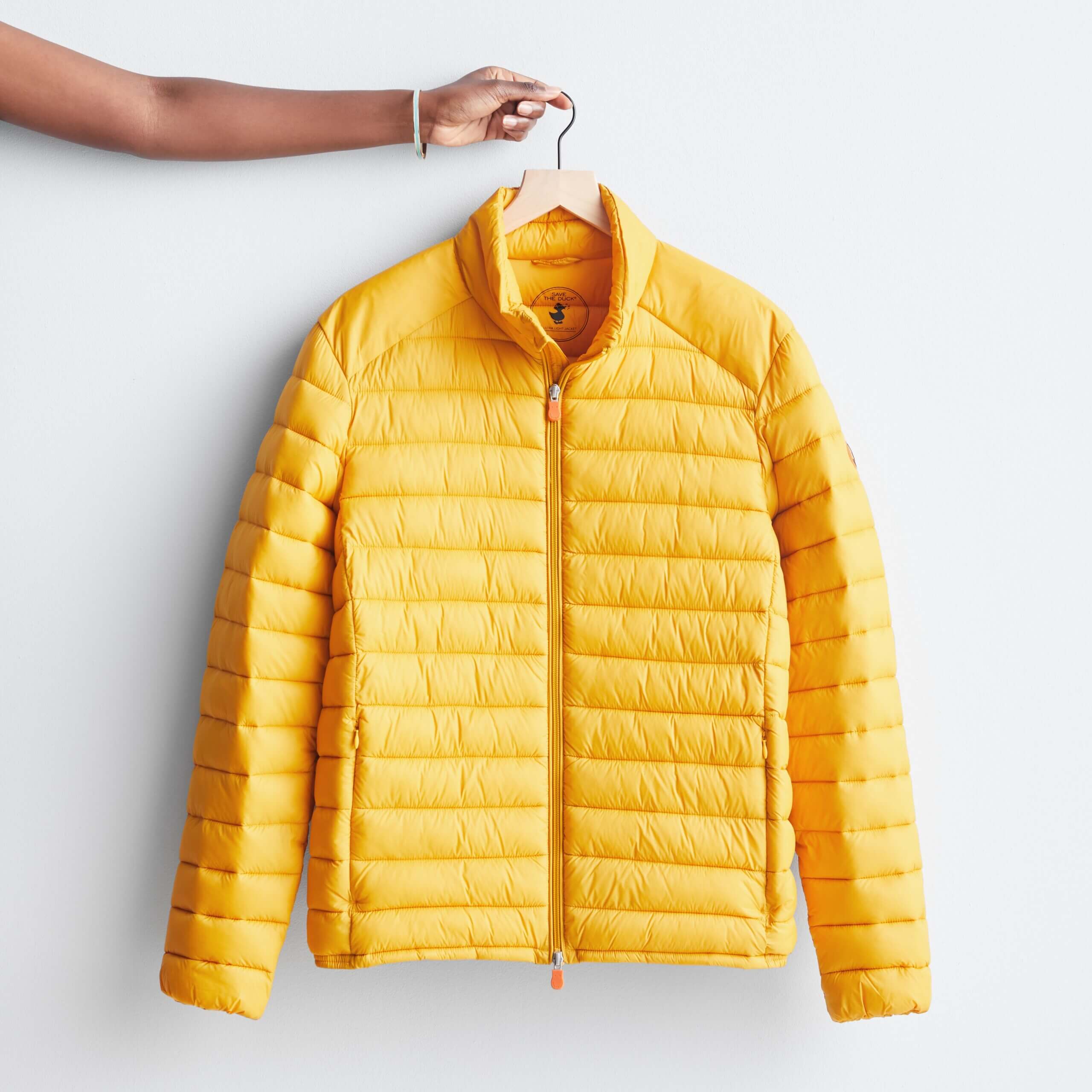 Stitch Fix men’s yellow puffer jacket on hanger held by hand.