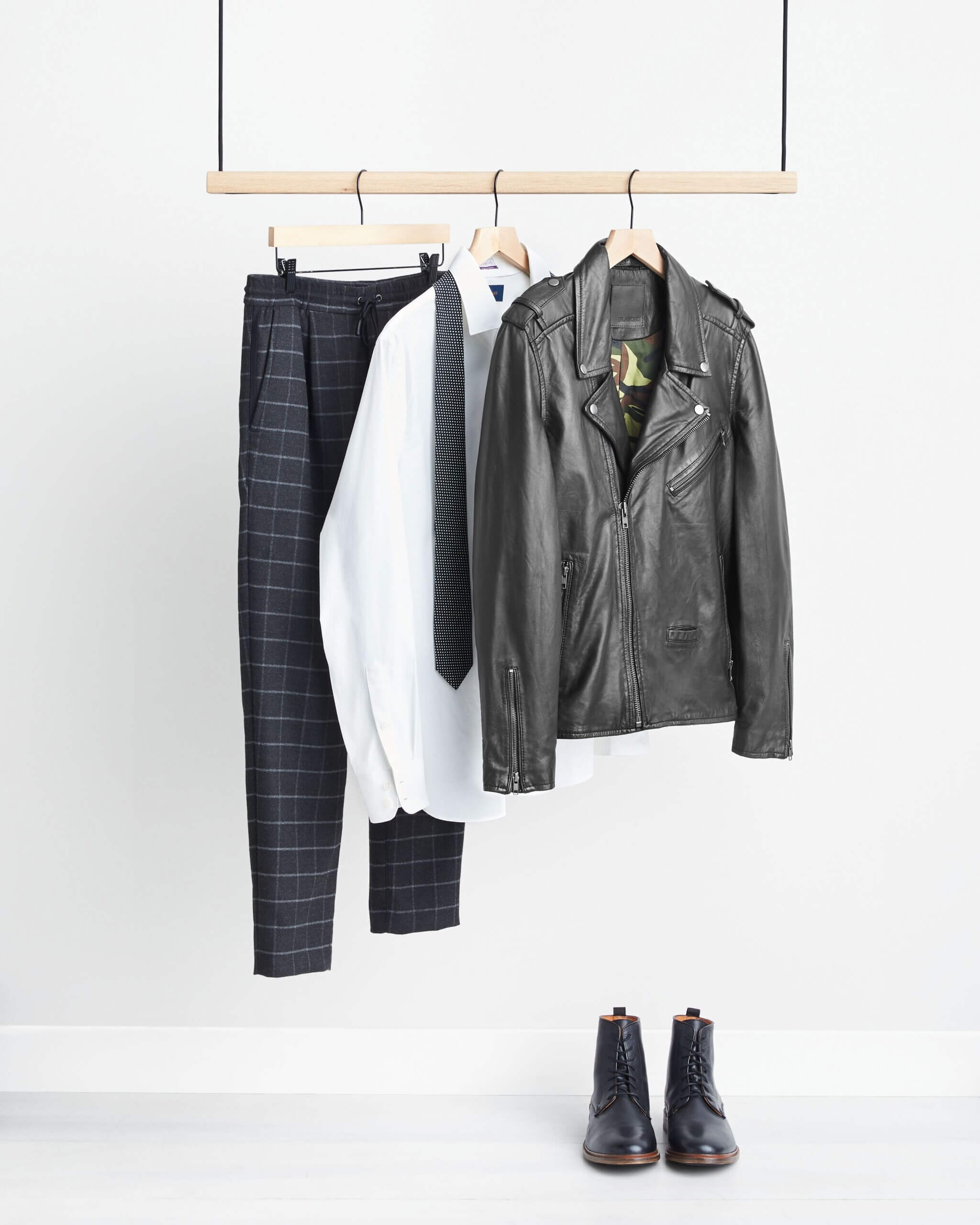 Stitch Fix men’s outfit on rack with black plaid pants, white button-down shirt, black printed tie, black leather moto jacket and black leather boots.