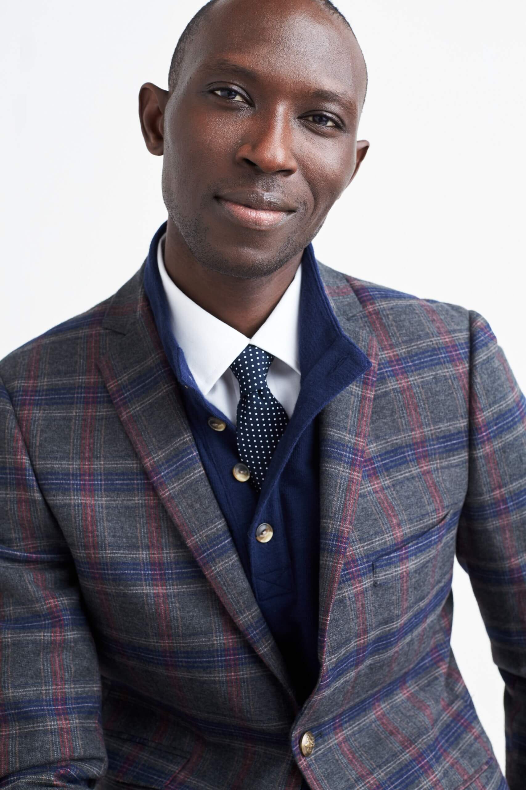 Stitch Fix model wearing men’s grey plaid blazer over blue button-down sweater, white button-up shirt and navy and white polka dot tie.