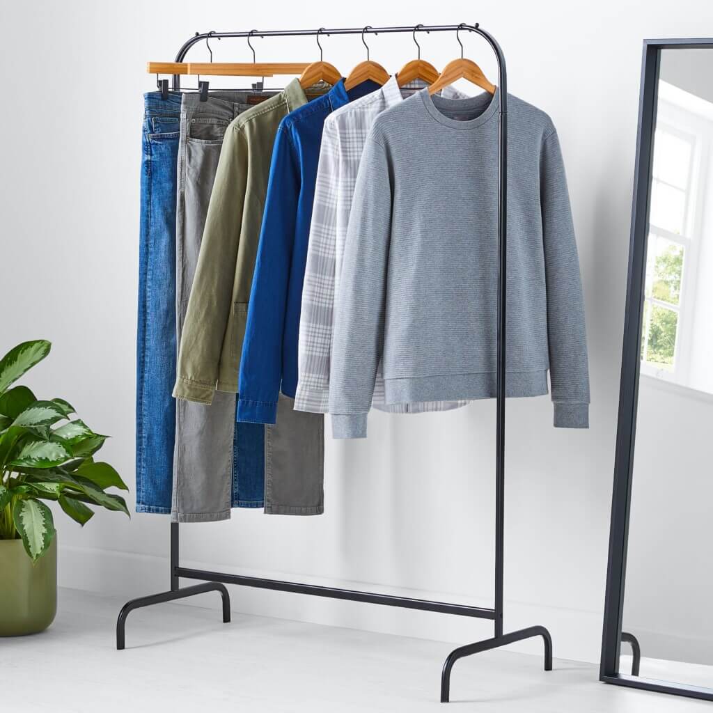 Stitch Fix men’s casual attire shirts and pants hanging on a rack next to a mirror and house plant.