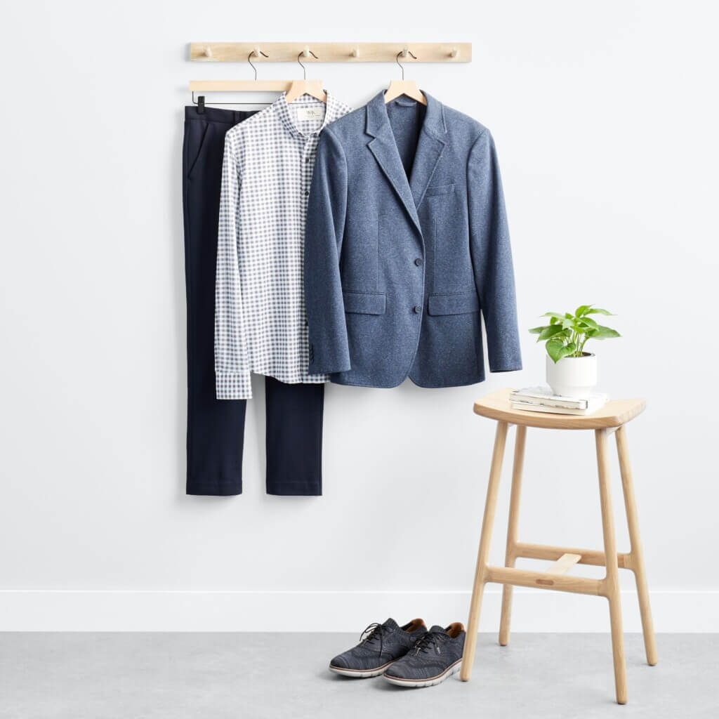 Stitch Fix men’s business casual outfit with plaid shirt, blue blazer, navy pants hanging next to stool with plant and books and navy shoes.