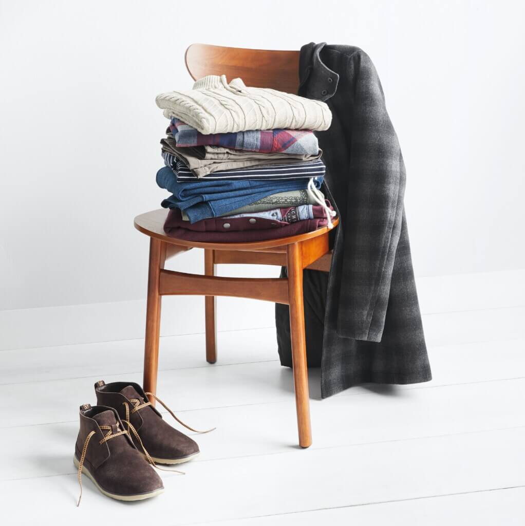 Stitch Fix men’s outfit for shorter men featuring shirts and sweaters stacked on chair with plaid jacket and brown chukka boots.
