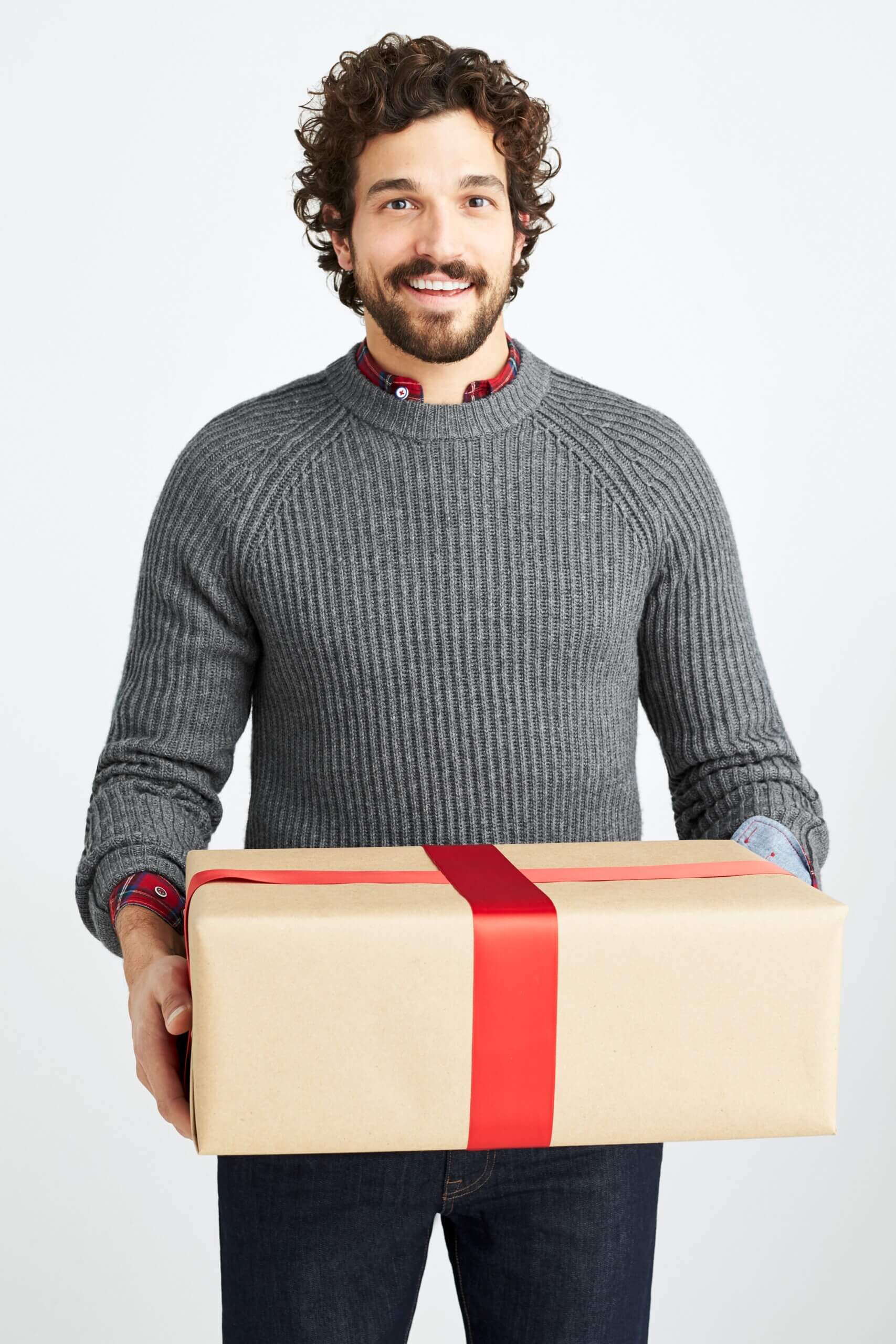 Stitch Fix men's Christmas outfit on model holding a present featuring grey sweater over red collared shirt and blue jeans.