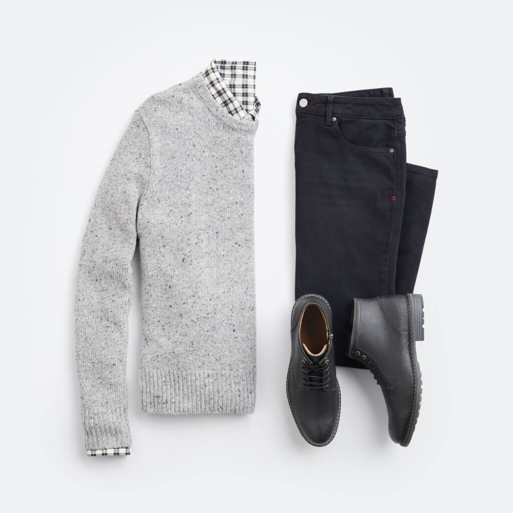 Stitch Fix men's New Year's Eve outfit featuring navy jacket chore jacket over gray sweater and navy and white plaid shirt, brown jeans and navy sneakers.