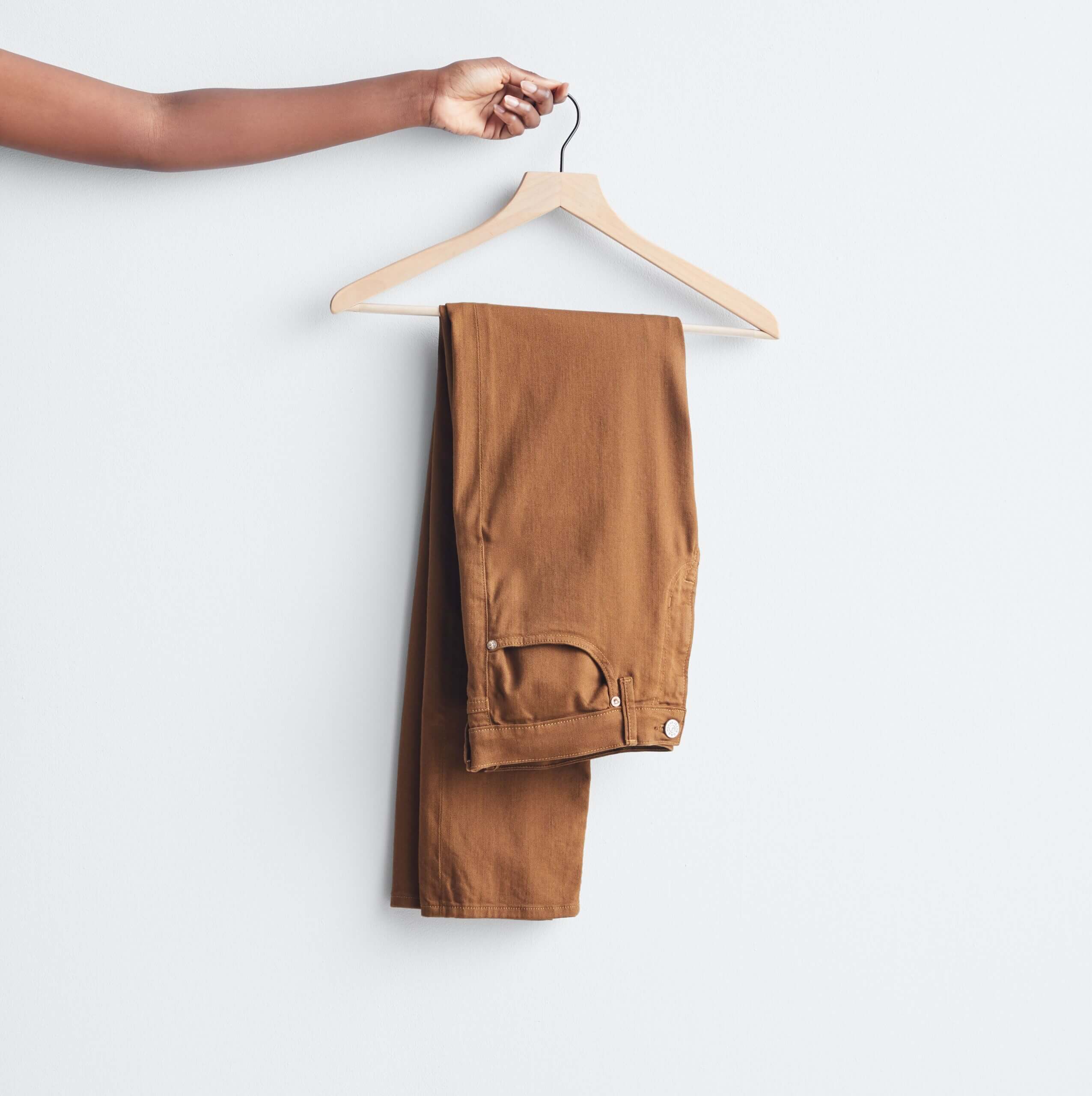 Stitch Fix model holding wooden hanger with brown jeans folded in half.