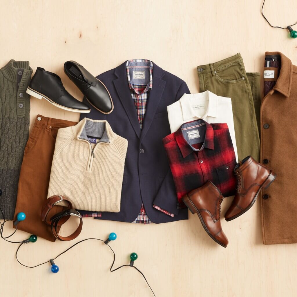 Stitch Fix men’s laydown featuring two sweaters, pants, boots, a blazer over plaid button-down shirt, collared shirts, jeans and jacket framed by Christmas lights.