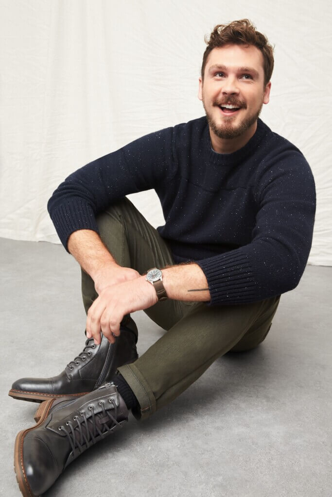 Stitch Fix model wearing men’s big and tall outfit with navy sweater, olive jeans, dark brown lace-up boots and wristwatch.