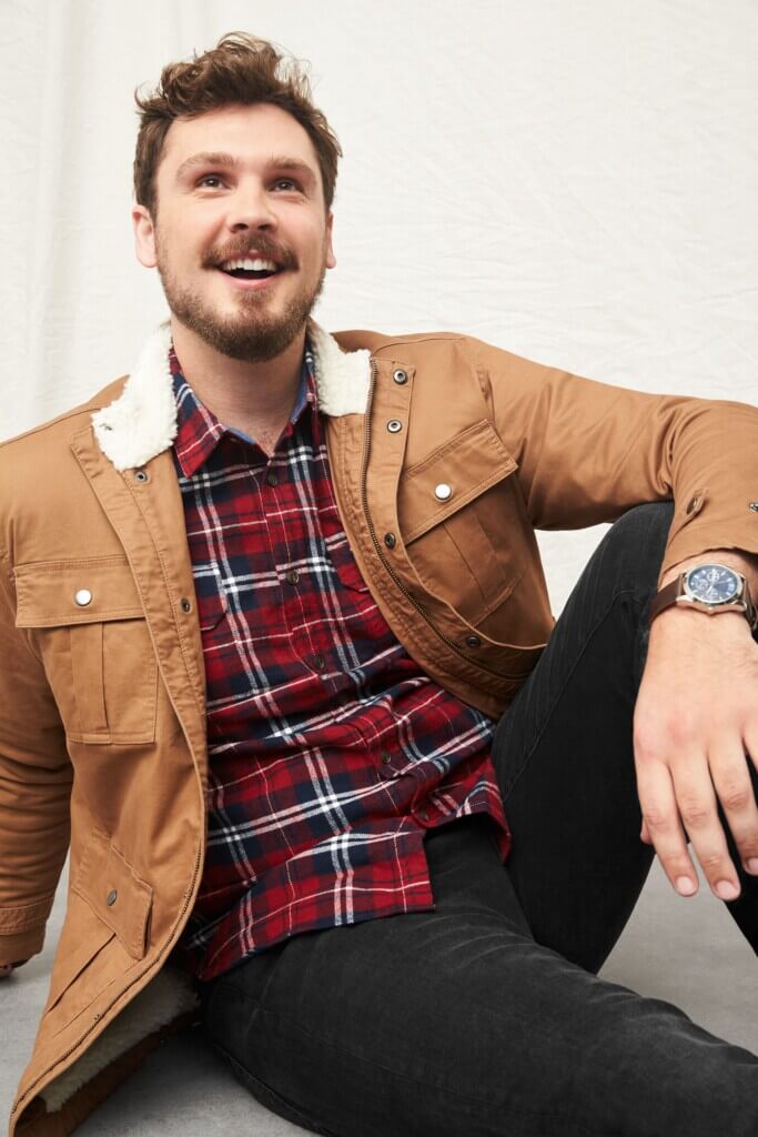 Stitch Fix model wearing Valentine's Day outfit for men featuring red plaid button-down, brown jacket over and black pants.