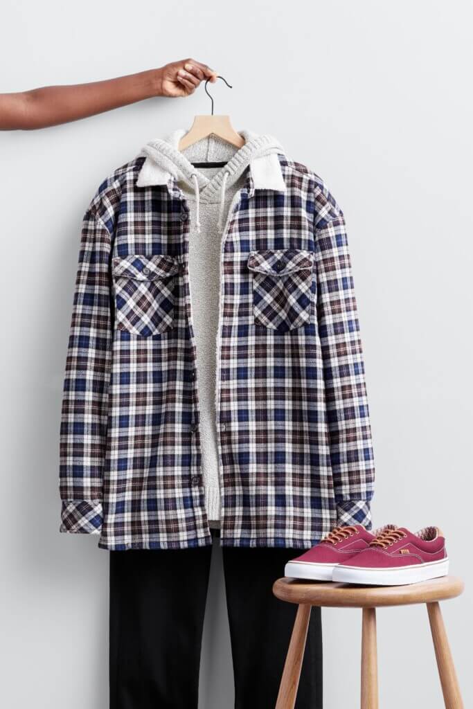 Stitch Fix Valentine's Day outfit for men featuring plaid shacket over hooded sweater and black jeans on hanger next to sneakers on stool.
