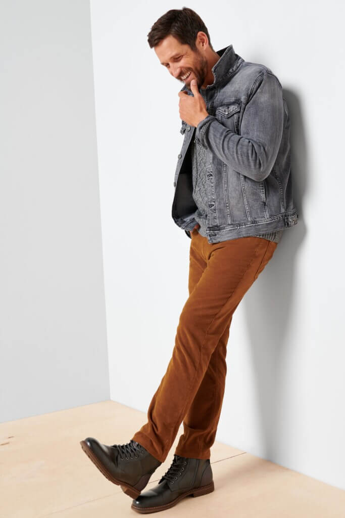 Stitch Fix Men's model wearing Valentine's Day outfit featuring grey jean jacket over grey sweater, brown pants and black boots.