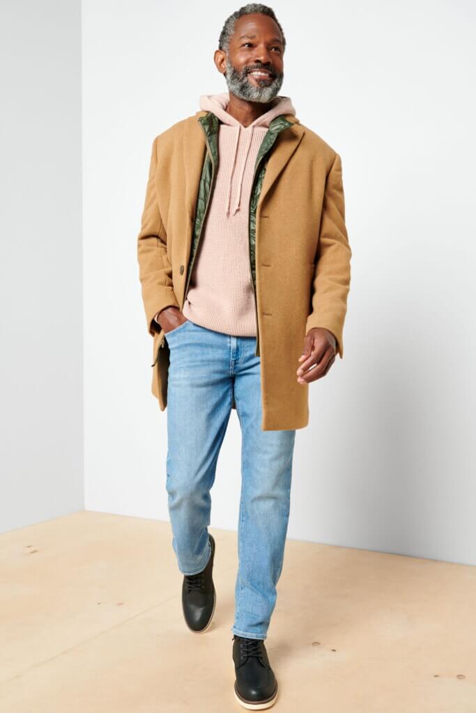 Stitch Fix Men’s model wearing Valentine’s Day outfit featuring hooded sweatshirt under coat, blue jeans and black boots.