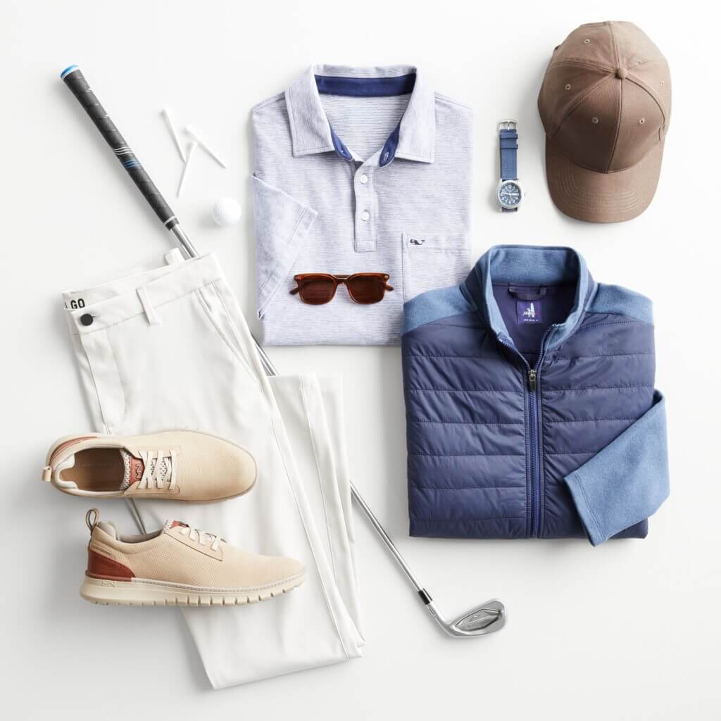 Stitch Fix men’s golf attire outfit featuring a blue polo, white pants and navy puffer jacket with a hat, sneakers, watch and golf equipment.