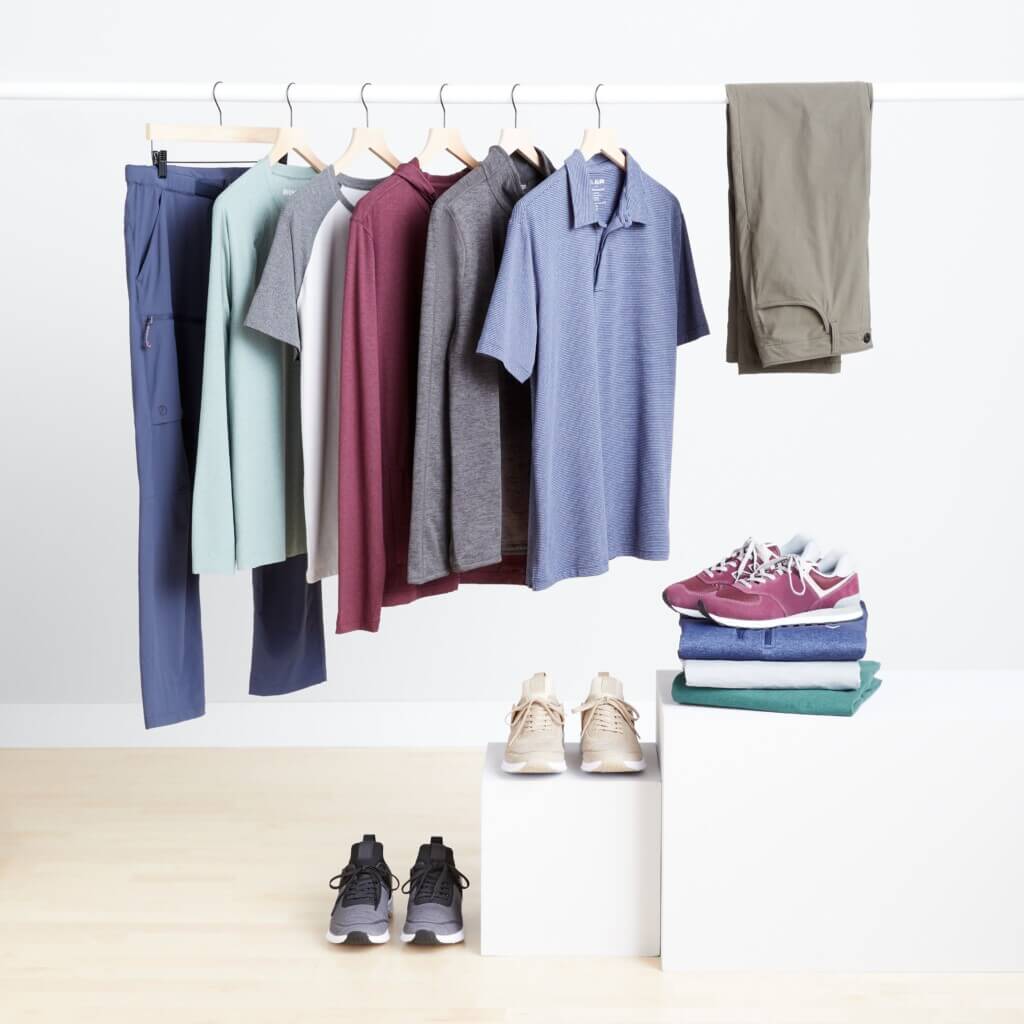 Stitch Fix men’s golf attire featuring polo shirts, pullovers and pants on rack with three pairs of sneakers displayed on the floor, a platform and on a stack of shirts.
