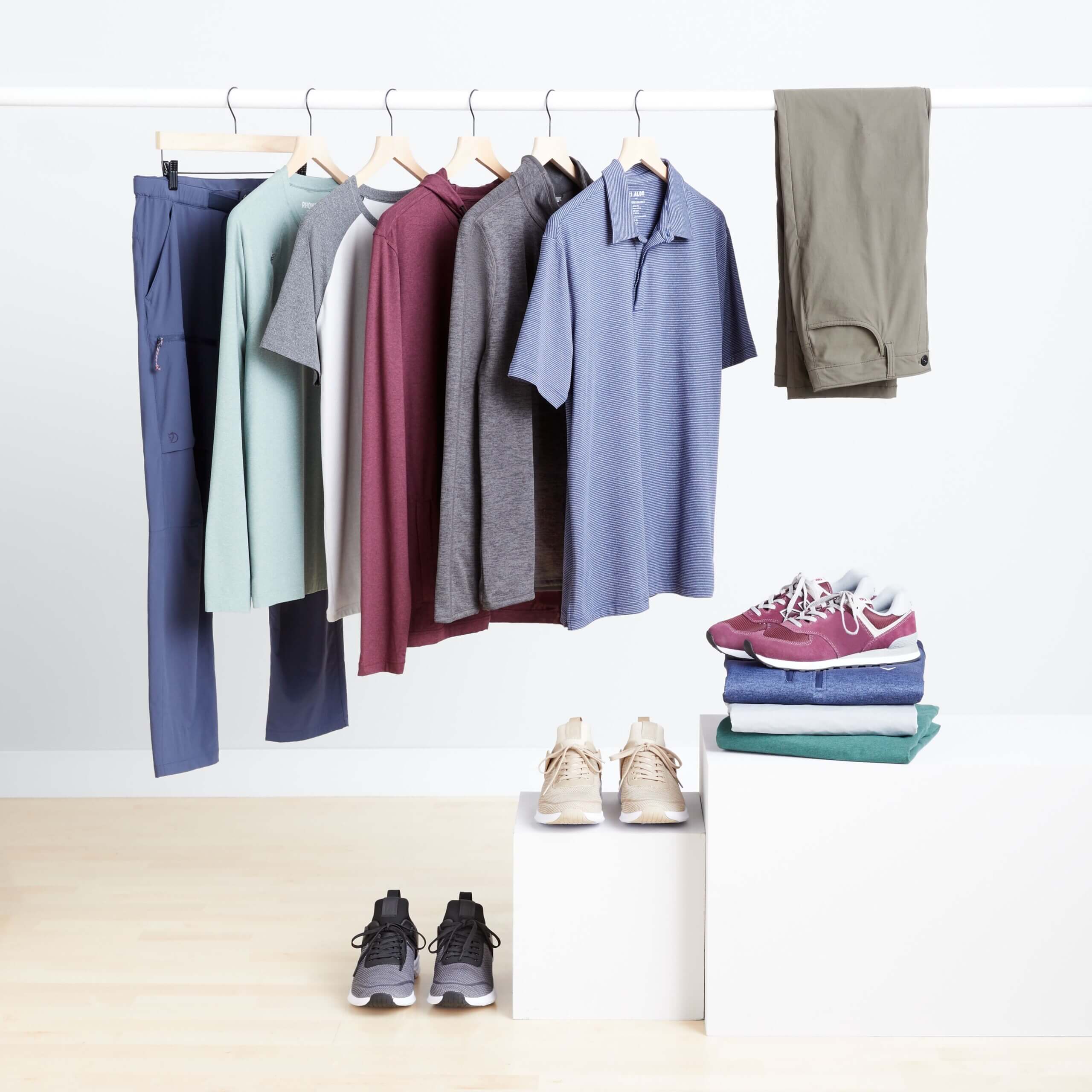 Stitch Fix men’s golf attire featuring polo shirts, pullovers and pants on rack with three pairs of sneakers displayed on the floor, a platform and on a stack of shirts.