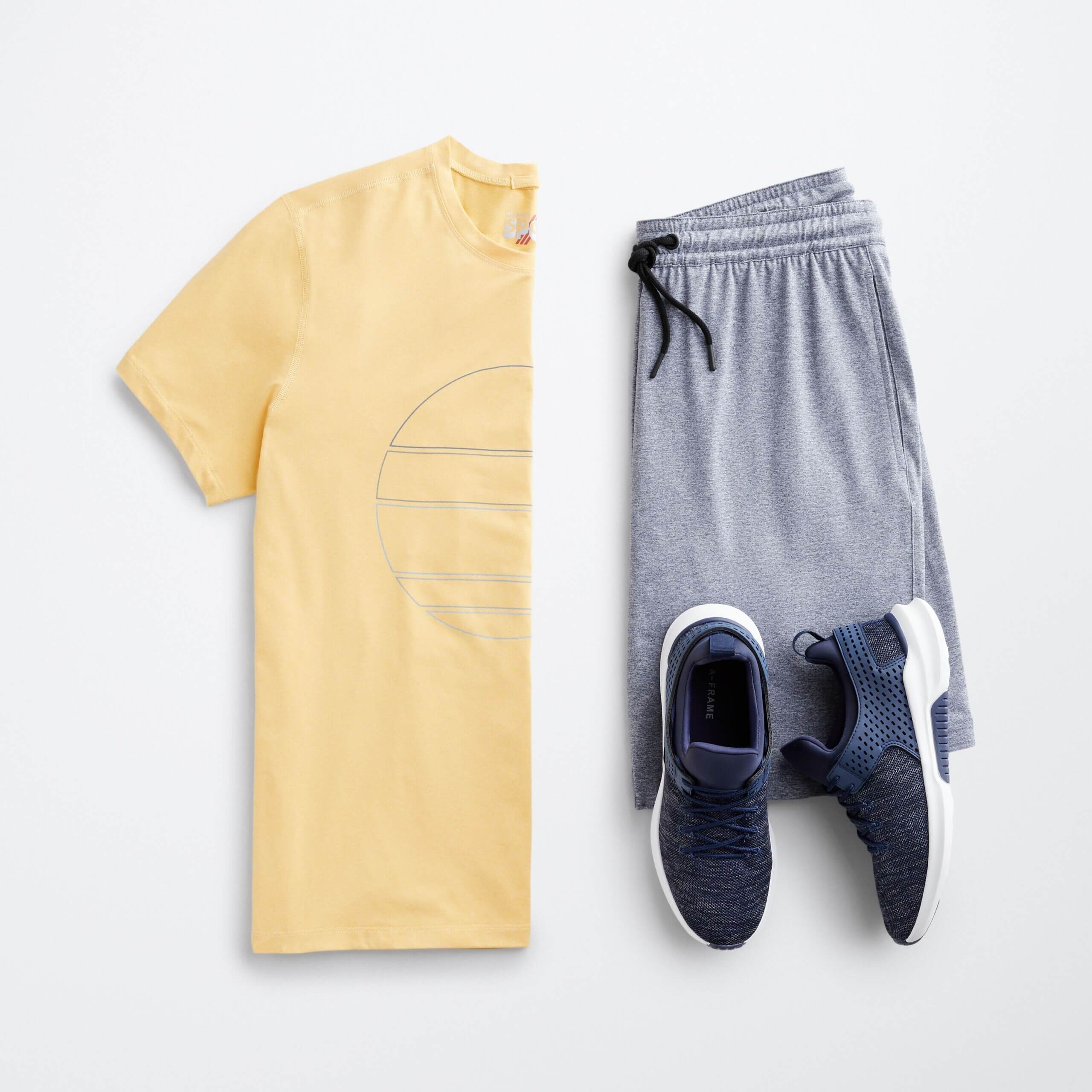 Stitch Fix men’s beach wear outfit featuring yellow graphic T-shirt, grey athletic shorts and navy sneakers.